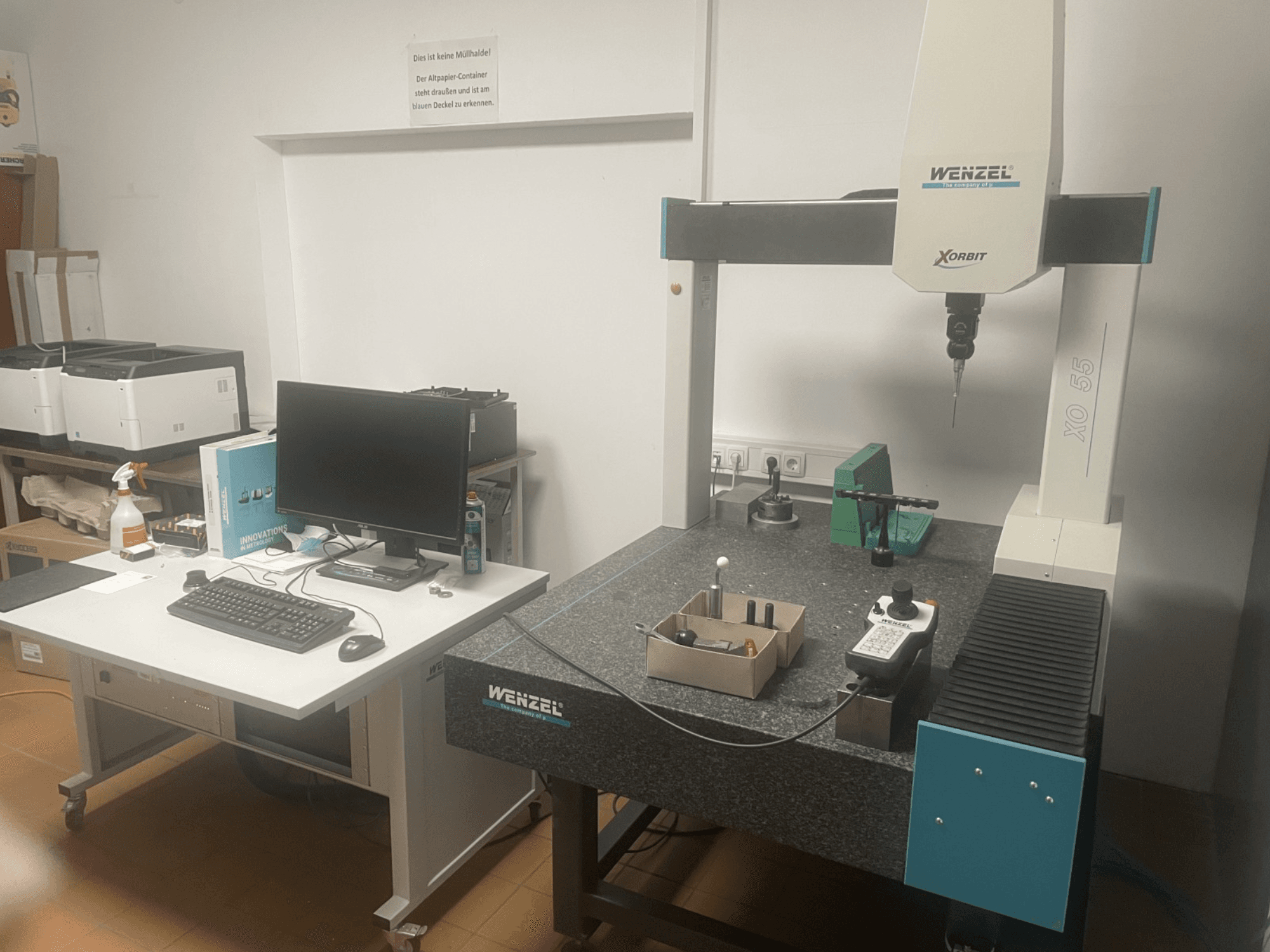 Machine à mesurer tridimensionnelle Wenzel XO 55 avec des outils verts sur une table en granit, vue de face avec un poste informatique.