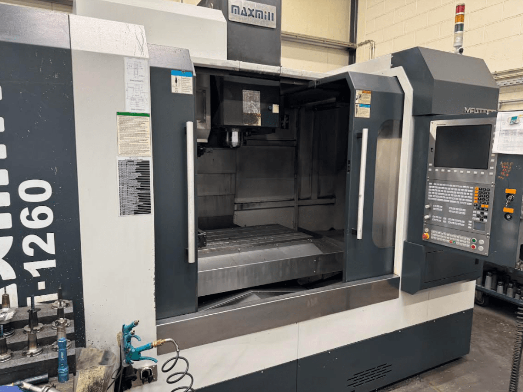 Fraiseuse CNC Maxmill, modèle M-1260, vue de face montrant l'espace de travail vide avec le panneau de commande et les instructions d'utilisation.