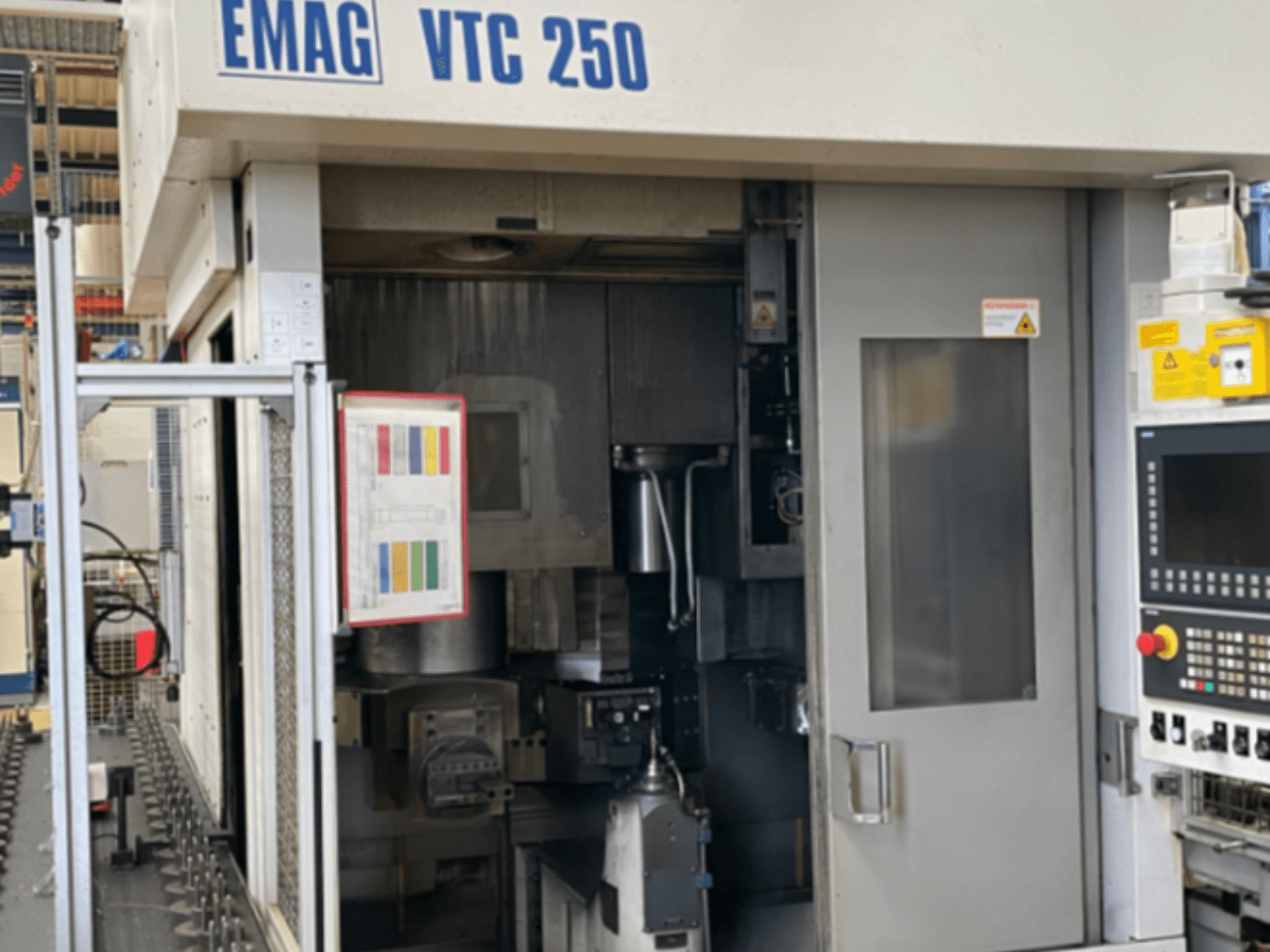 Vue de face du tour vertical EMAG VTC 250, montrant le panneau de commande, l'interface utilisateur et la porte d'accès ouverte.