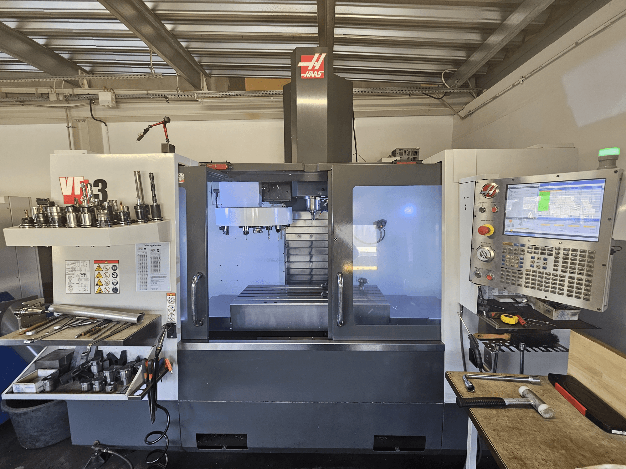 Machine CNC Haas VF-3 dans un atelier, vue de face montrant les outils, les commandes et la zone de fraisage avec intérieur éclairé.