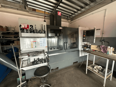 Machine CNC Haas VF-3 dans un atelier, vue de face avec les outils et les commandes sur la table adjacente, affichant l'interface technique et les informations de sécurité.