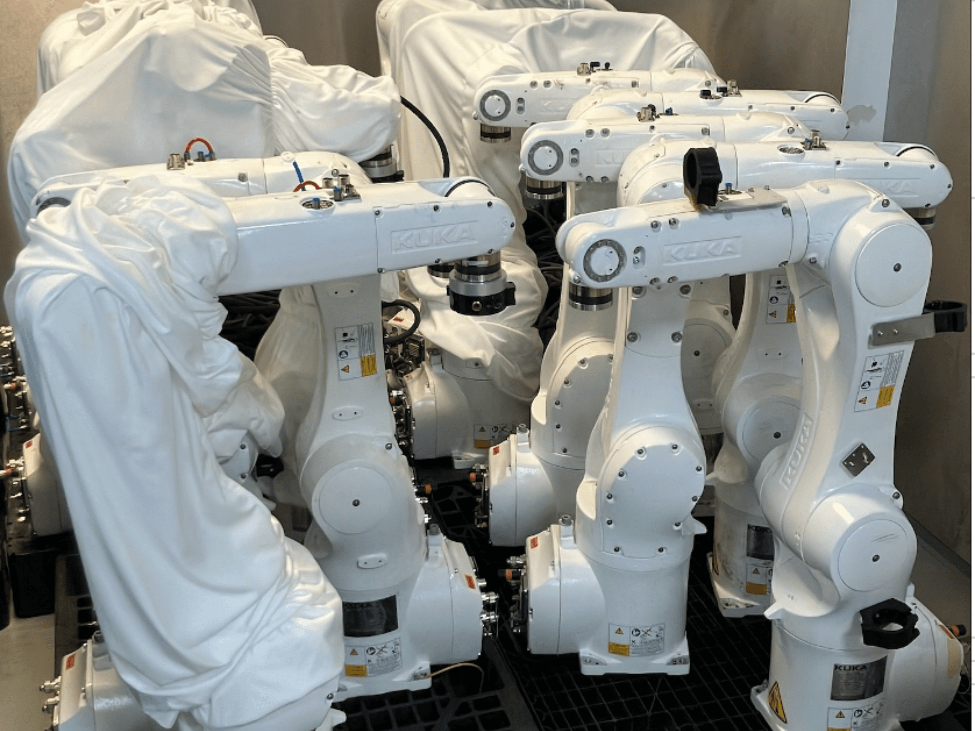 Bras robotiques KUKA KR 10 R900-2 recouverts de tissu blanc, vus d'un angle supérieur, montrant plusieurs unités en stockage.