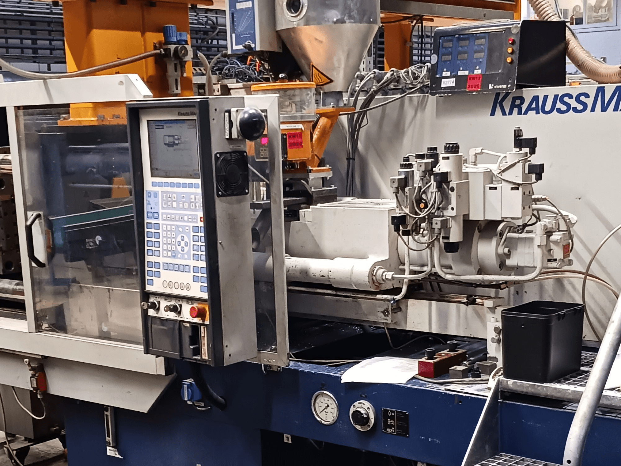 Machine de moulage par injection KraussMaffei avec panneau de commande, unités hydrauliques et outils au premier plan, vue de face.