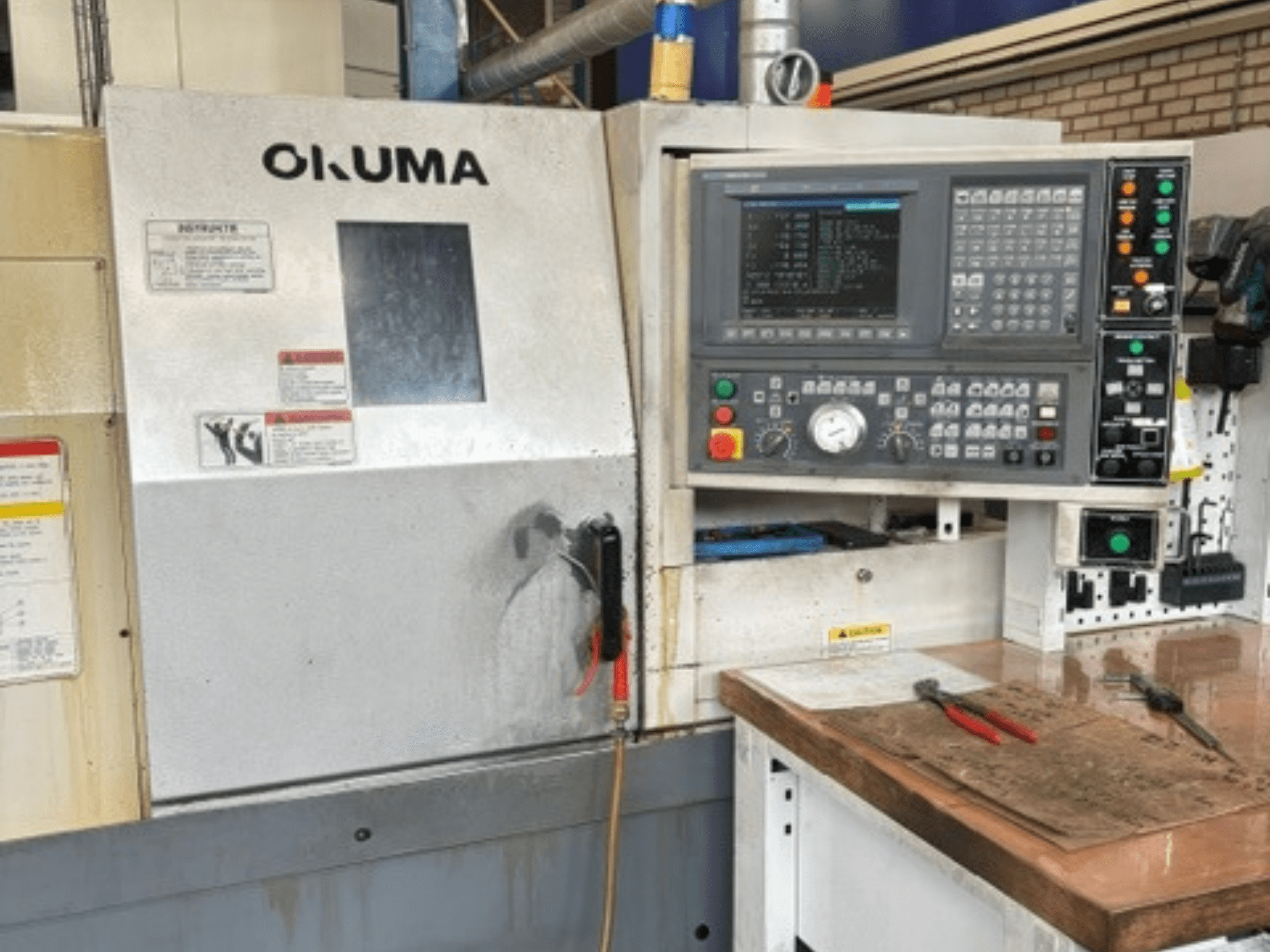 Vue de face du tour horizontal Okuma ES-L10II, montrant le panneau de commande, l'écran et la zone de travail avec les outils.