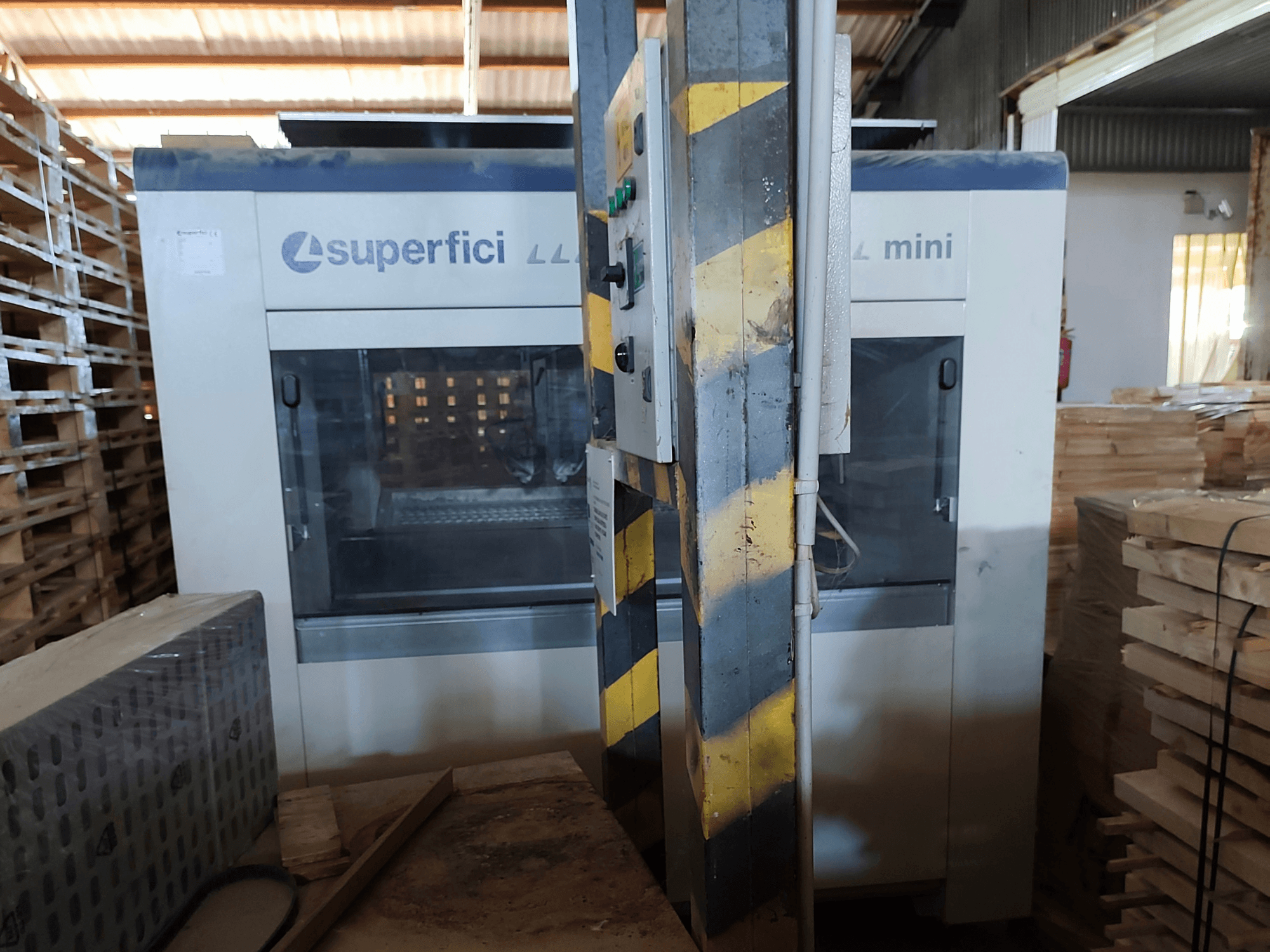 Vue de face de la machine de finition du bois SCM Superfici Mini, montrant le tableau de commande et les palettes en bois qui l'entourent.