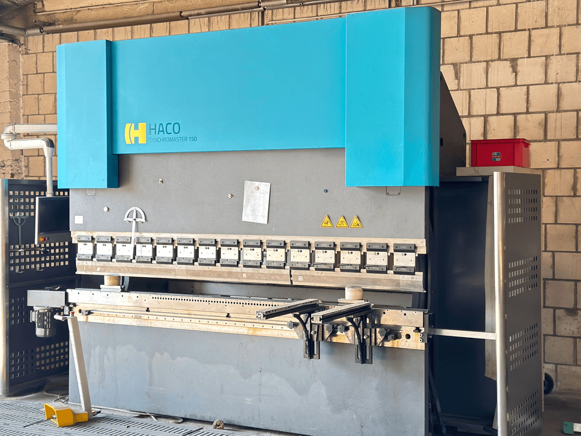 Presse plieuse HACO SRM30150, vue de face ; comprend le panneau de commande et les matrices de serrage, avec les étiquettes d'avertissement de sécurité visibles.
