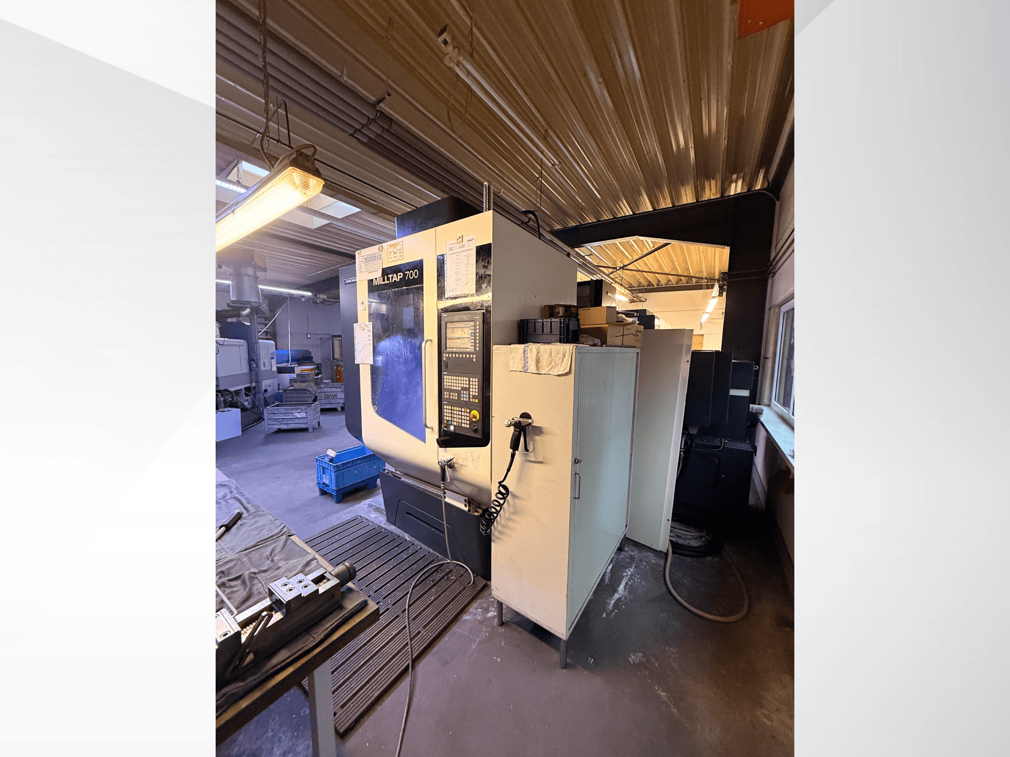 Machine CNC Milltap 700 dans l'atelier ; la vue de face montre le panneau de commande, les supports d'outils et les zones de stockage avec l'éclairage au-dessus.