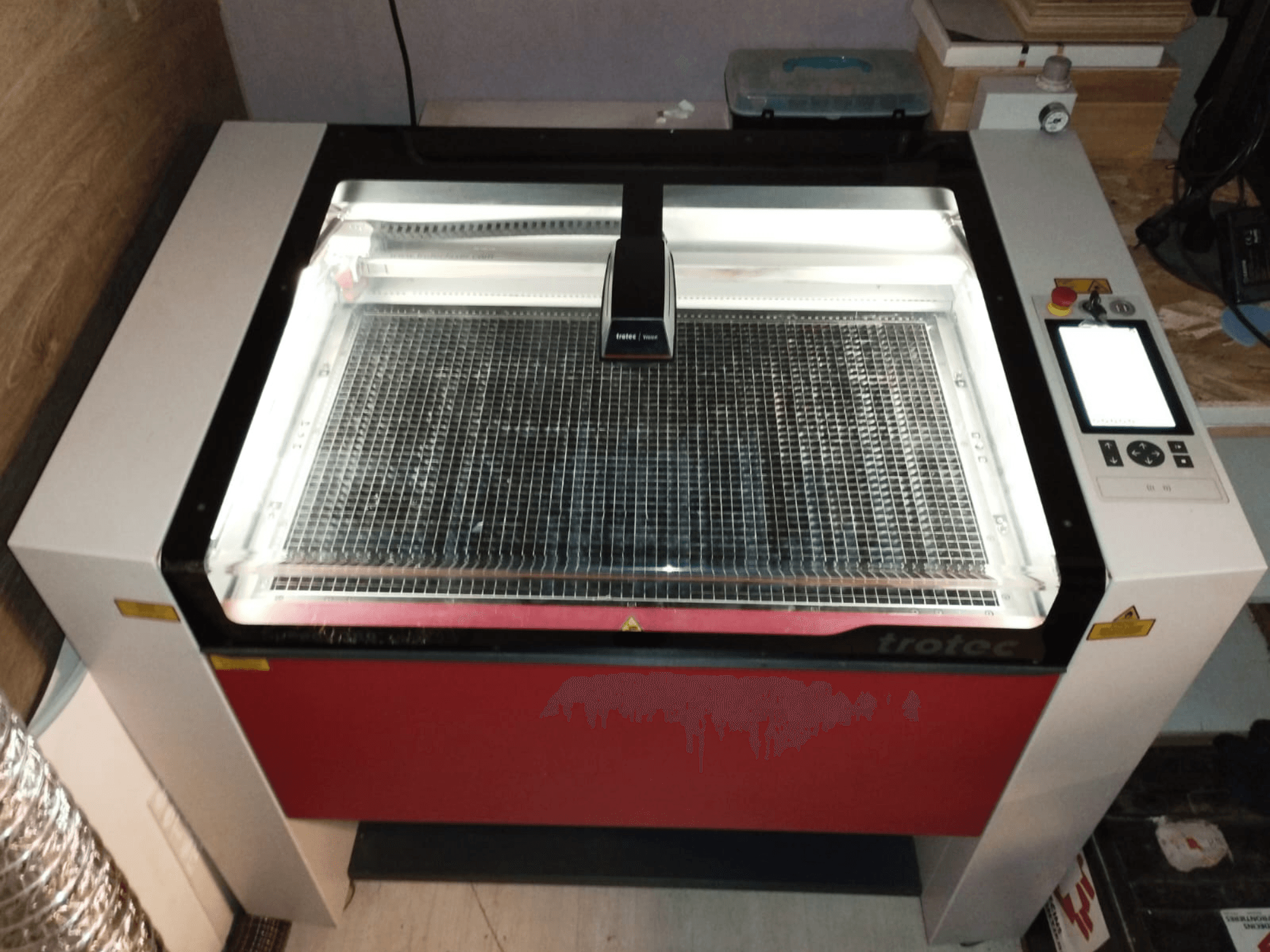 Découpeur laser Trotec avec un couvercle transparent, un lit de grille et un panneau de commande à droite ; vue de face montrant la conception et les caractéristiques.