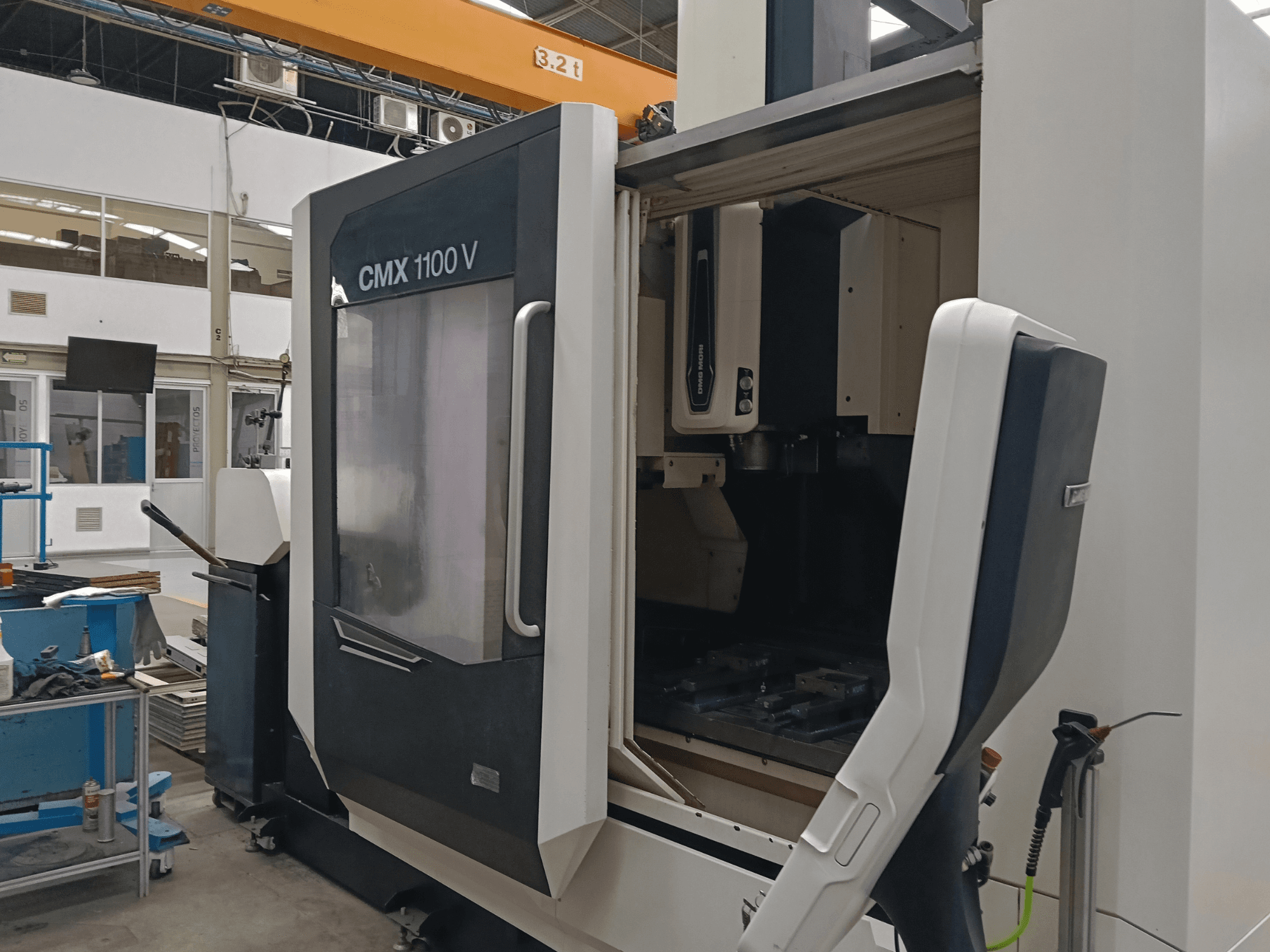 Centre d'usinage vertical DMG MORI CMX 1100 V, vue de face montrant la porte ouverte et la configuration interne de l'outillage dans un espace industriel.