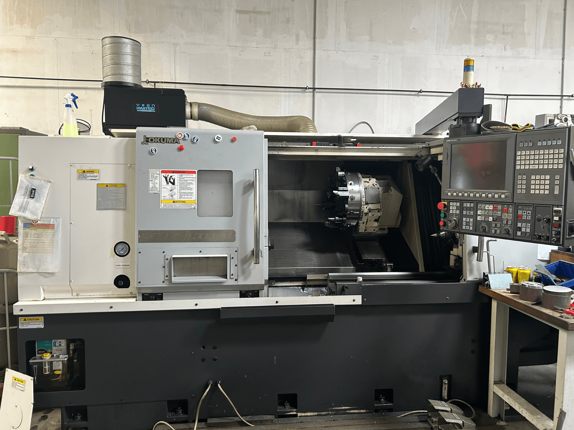 Vue avant d'un tour horizontal Okuma Genos L300E-M avec panneau de commande, broche visible et divers outils de réglage.