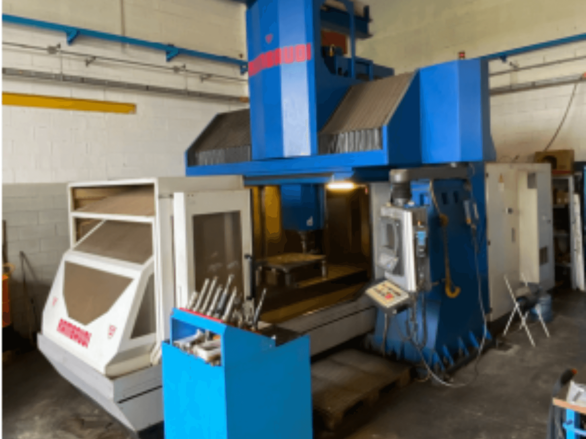 Centre d'usinage vertical Rambaudi RF103, vue de face montrant les commandes, le stockage des outils et la zone d'usinage. Extérieur bleu et blanc.