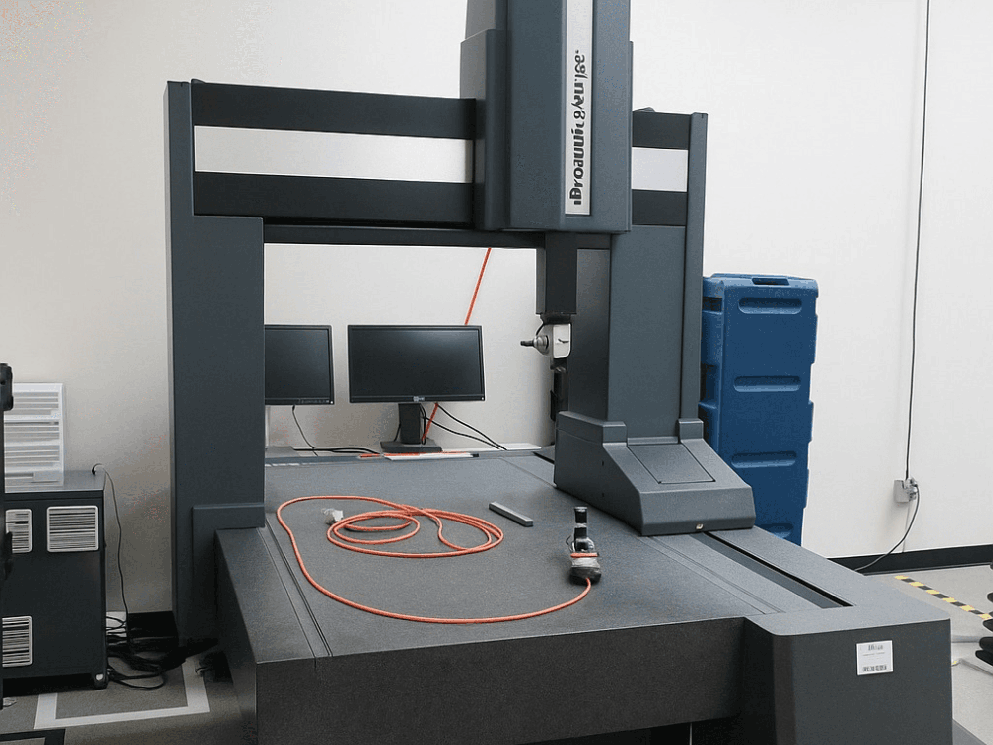 Machine à mesurer tridimensionnelle Brooks Automation avec deux moniteurs, vue de face, dotée d'un plateau gris et d'outils de mesure.