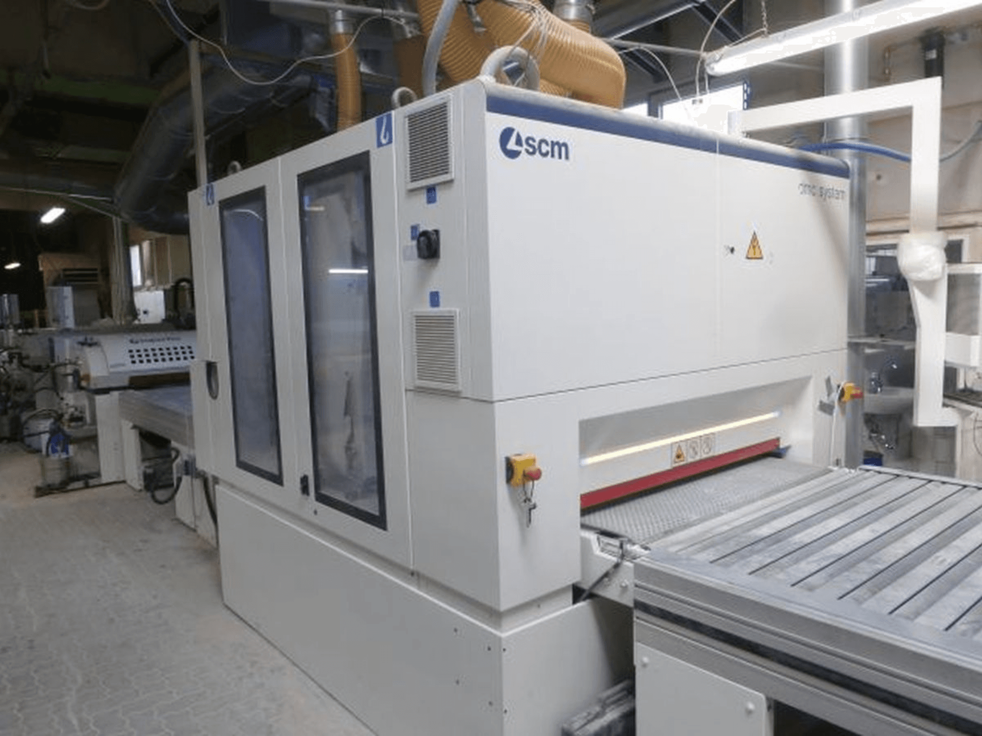 Ponceuse à bande SCM DMC SY TC 1350 dans un atelier, vue de profil montrant le panneau de commande et la surface de ponçage avec ses dispositifs de sécurité.
