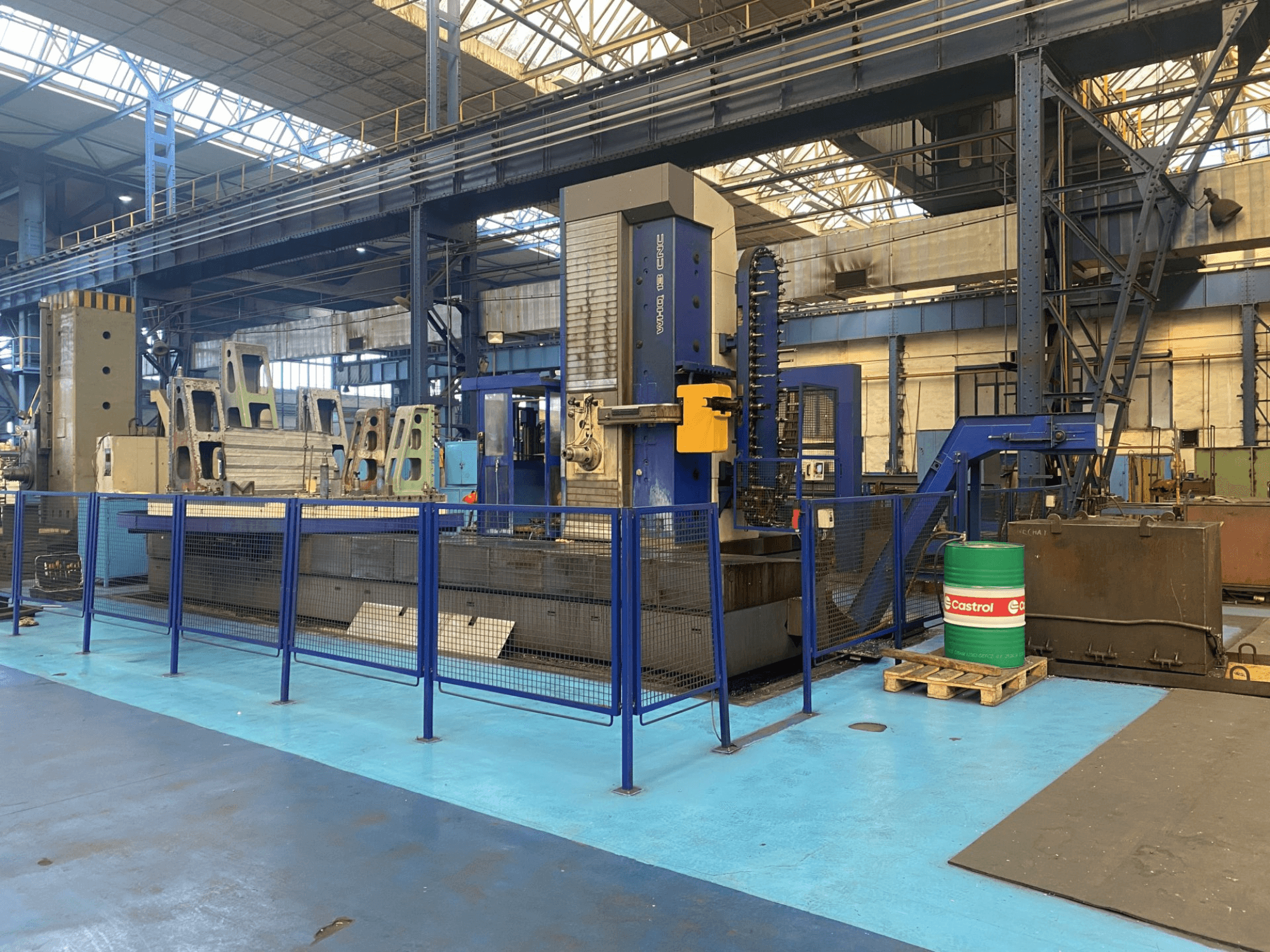 Aléseuse CNC TOS WHQ 13 dans un atelier, vue de face, montrant le cadre bleu et la barrière de sécurité qui l'entoure.