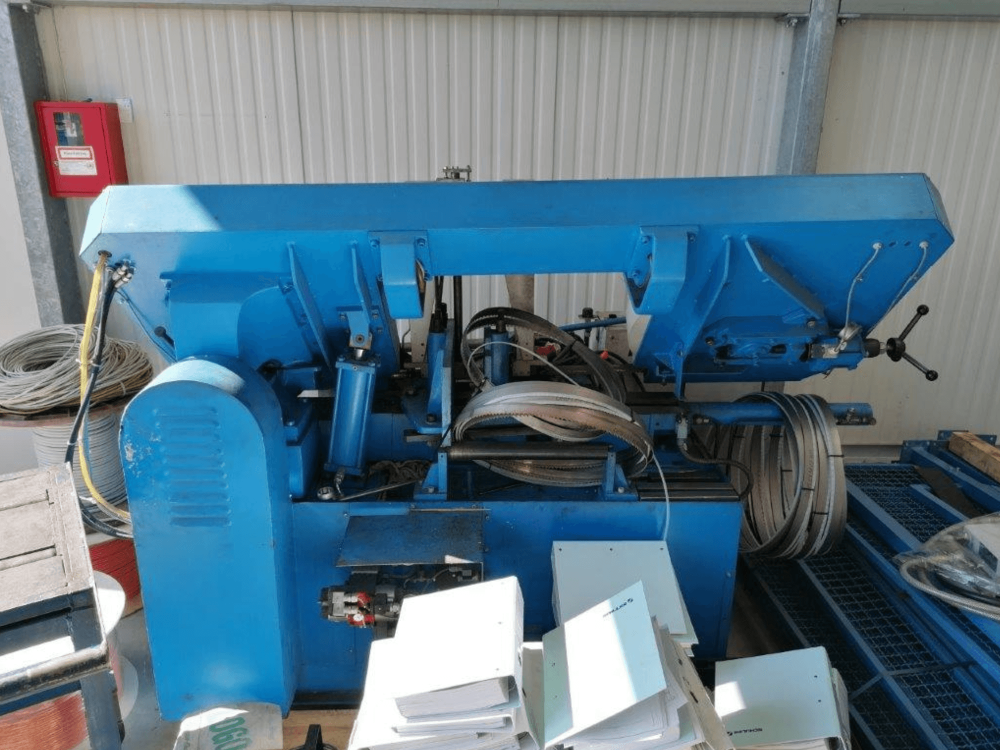 Machine industrielle bleue avec des composants hydrauliques, vue de côté, comprenant des tuyaux et des feuilles de métal sur une surface.
