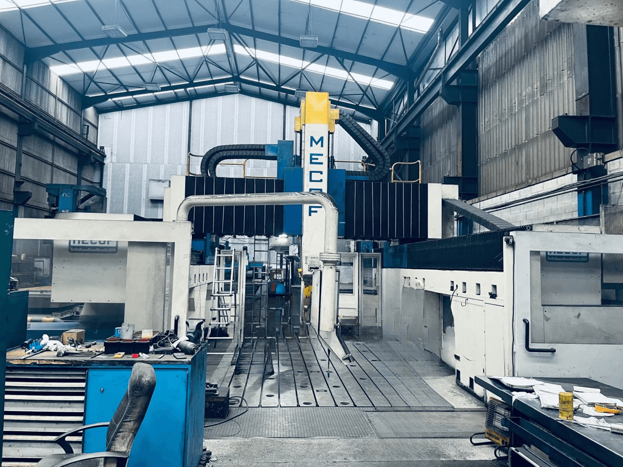 Fraiseuse à portique MECOF DYNAMILL 3000L dans l'atelier, vue de face, mettant en évidence la structure bleue et blanche, les outils et l'espace de travail.