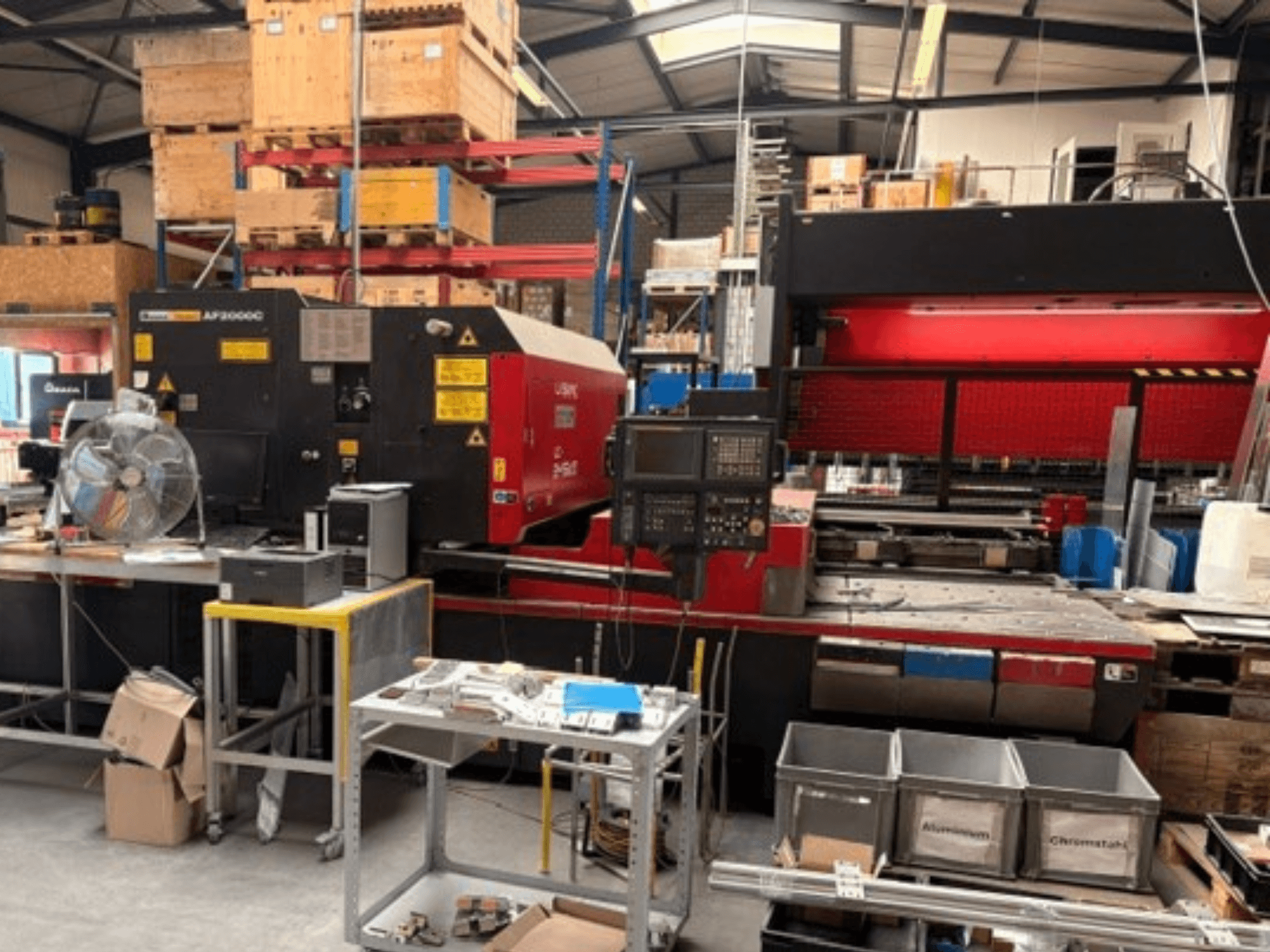 Machine de découpe laser CO₂ AMADA LC-2415αIII dans un atelier, avec vue de face, panneau de commande et espace de travail.
