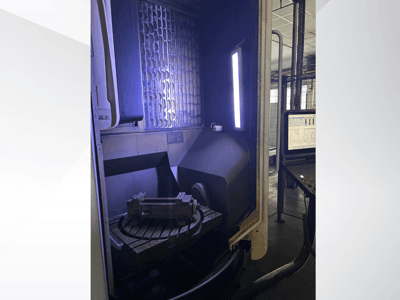 Centre d'usinage vertical DMG MORI DMU 65 MonoBlock, vue de face montrant la table rotative avec la pièce à usiner et le panneau de commande.