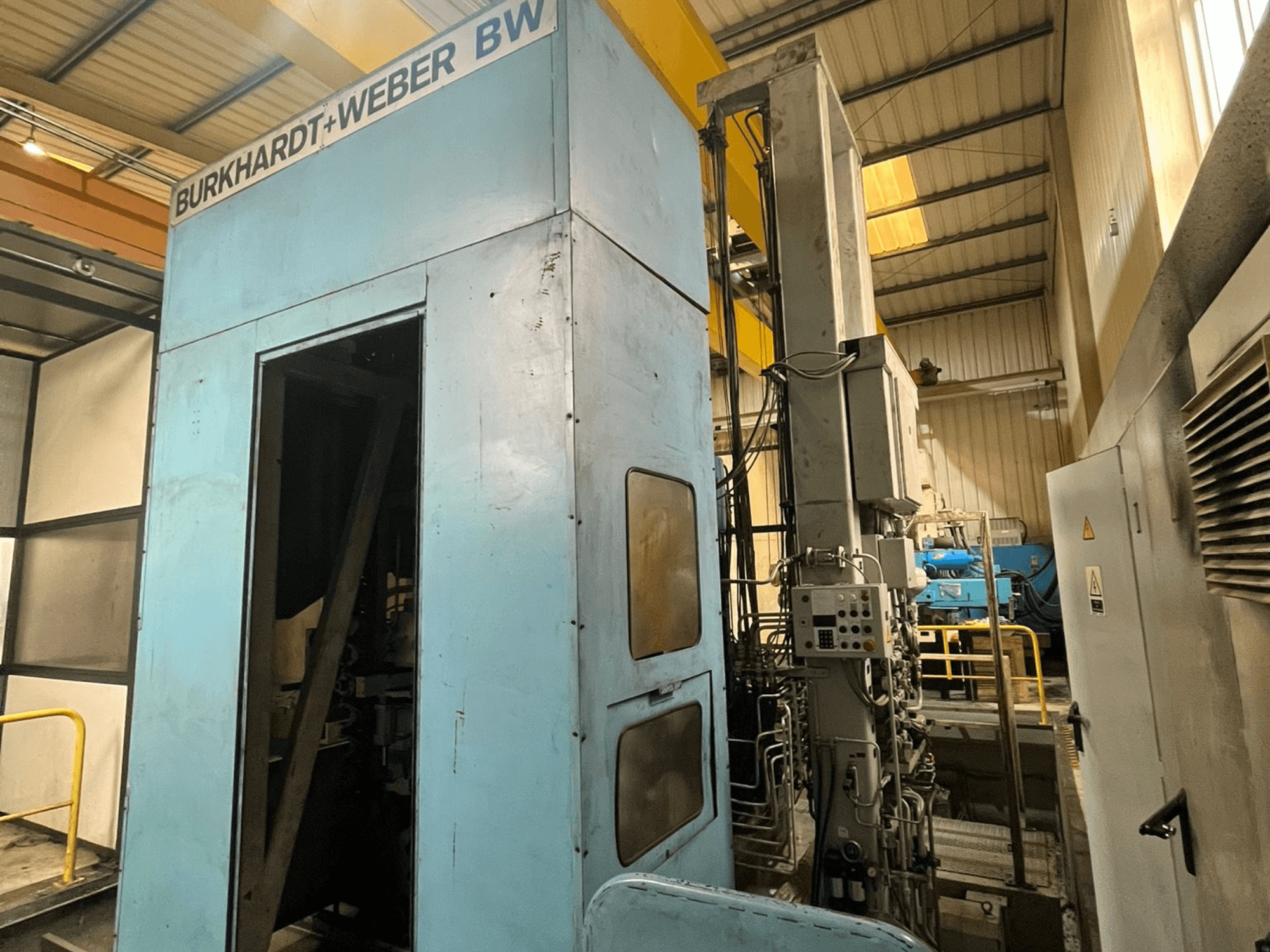 Centre d'usinage horizontal Burkhardt-Weber MC100, vue de profil montrant la carrosserie bleue et le panneau de commande avec les tuyaux apparents.