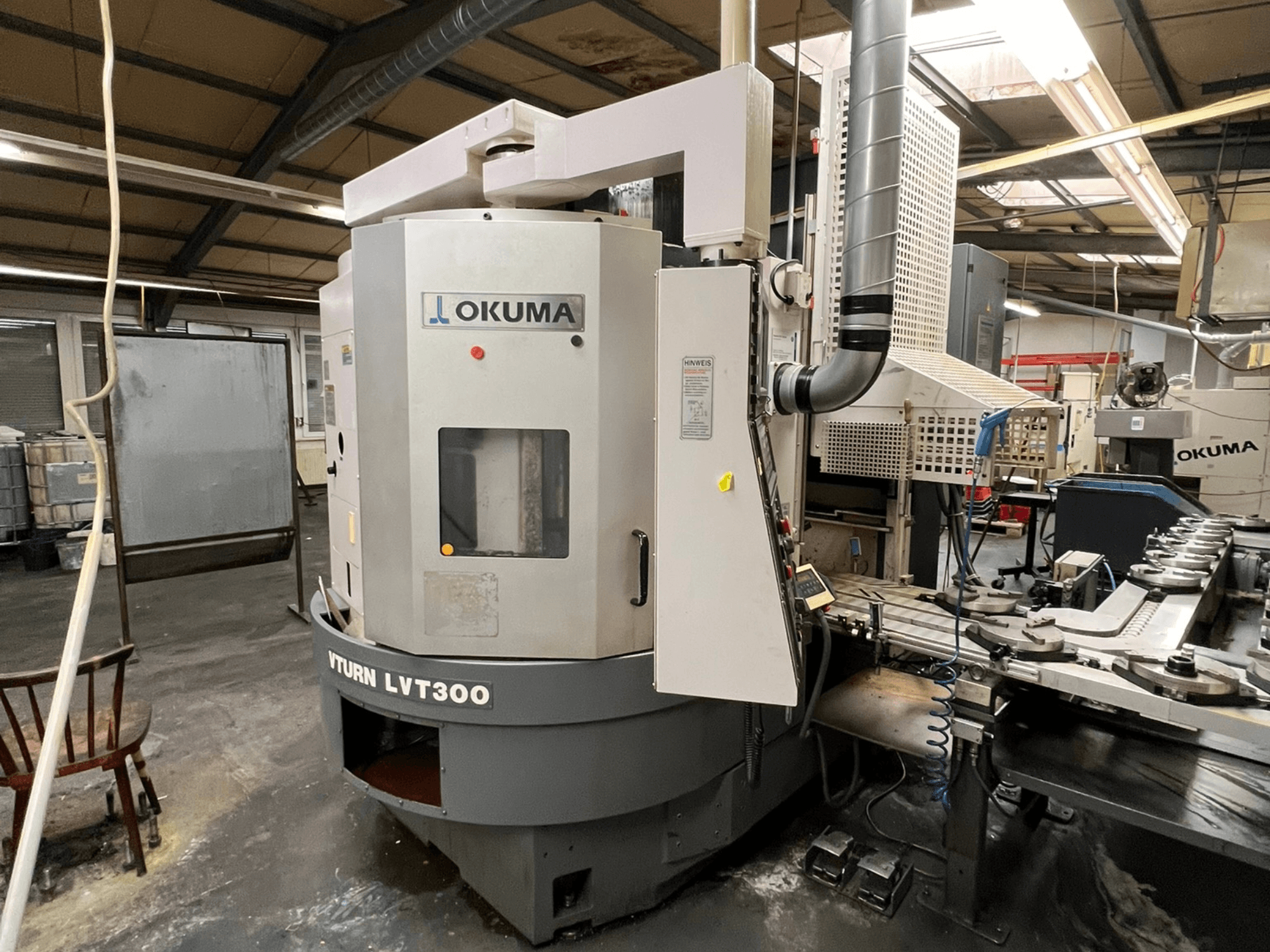 Tour CNC Okuma Vturn LVT300, vue latérale dans un environnement industriel, montrant le panneau de commande et le système de refroidissement.
