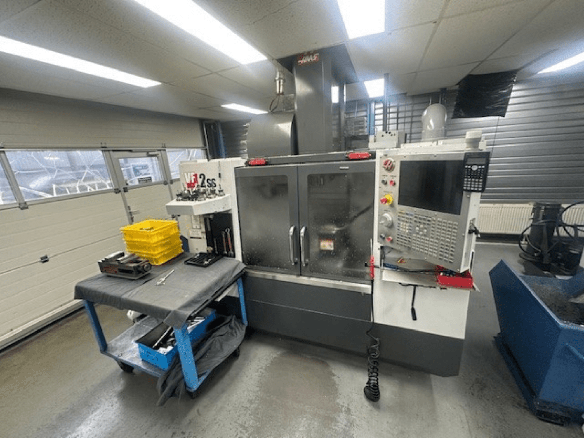 Vue avant du centre d'usinage vertical HAAS VF-2SS avec le panneau de commande, la table de travail et la station de stockage des outils.