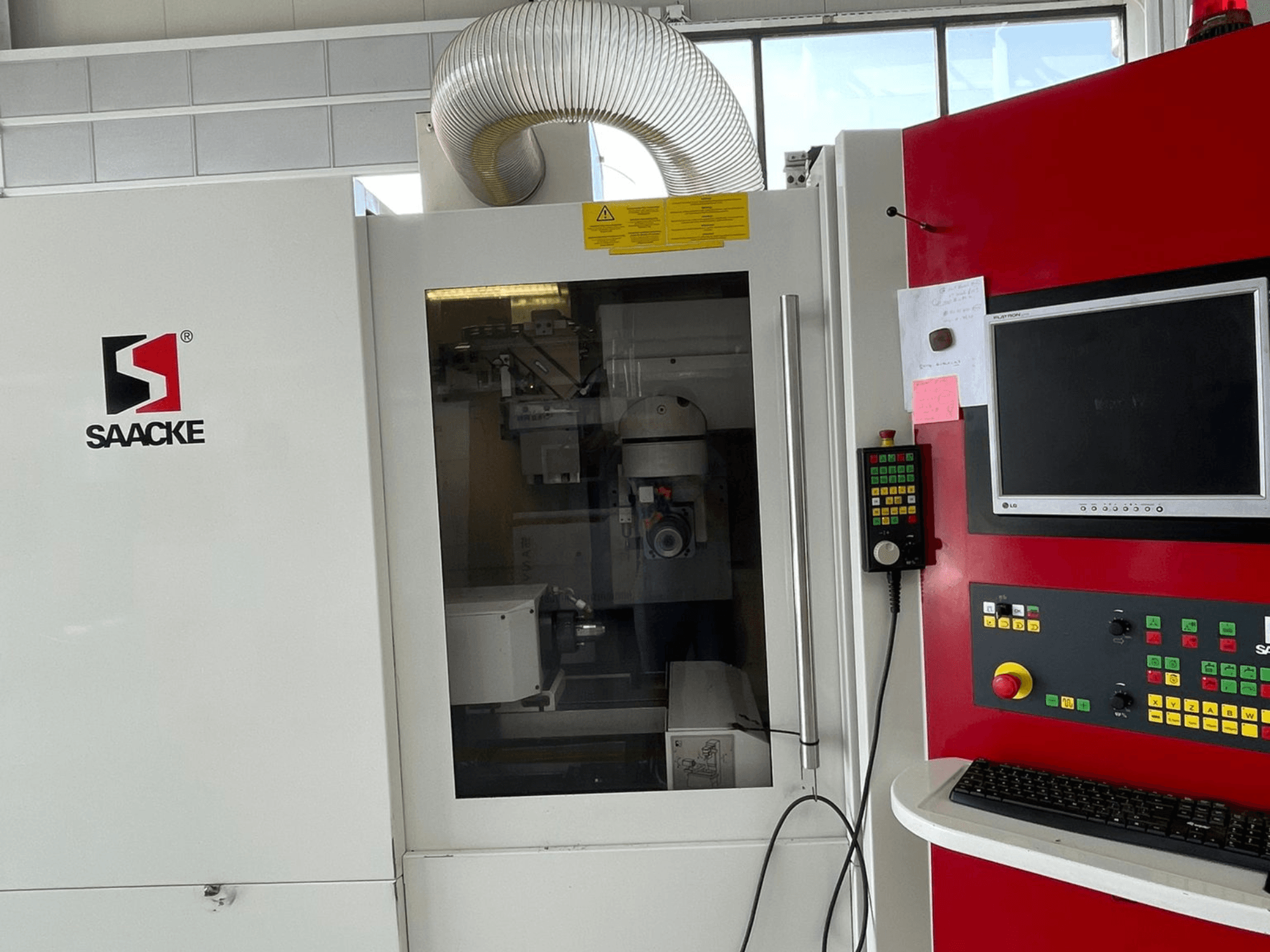 Machine SAACKE blanche et rouge, vue de face, comportant un panneau de commande, un moniteur et des parties internes visibles à travers la vitre.
