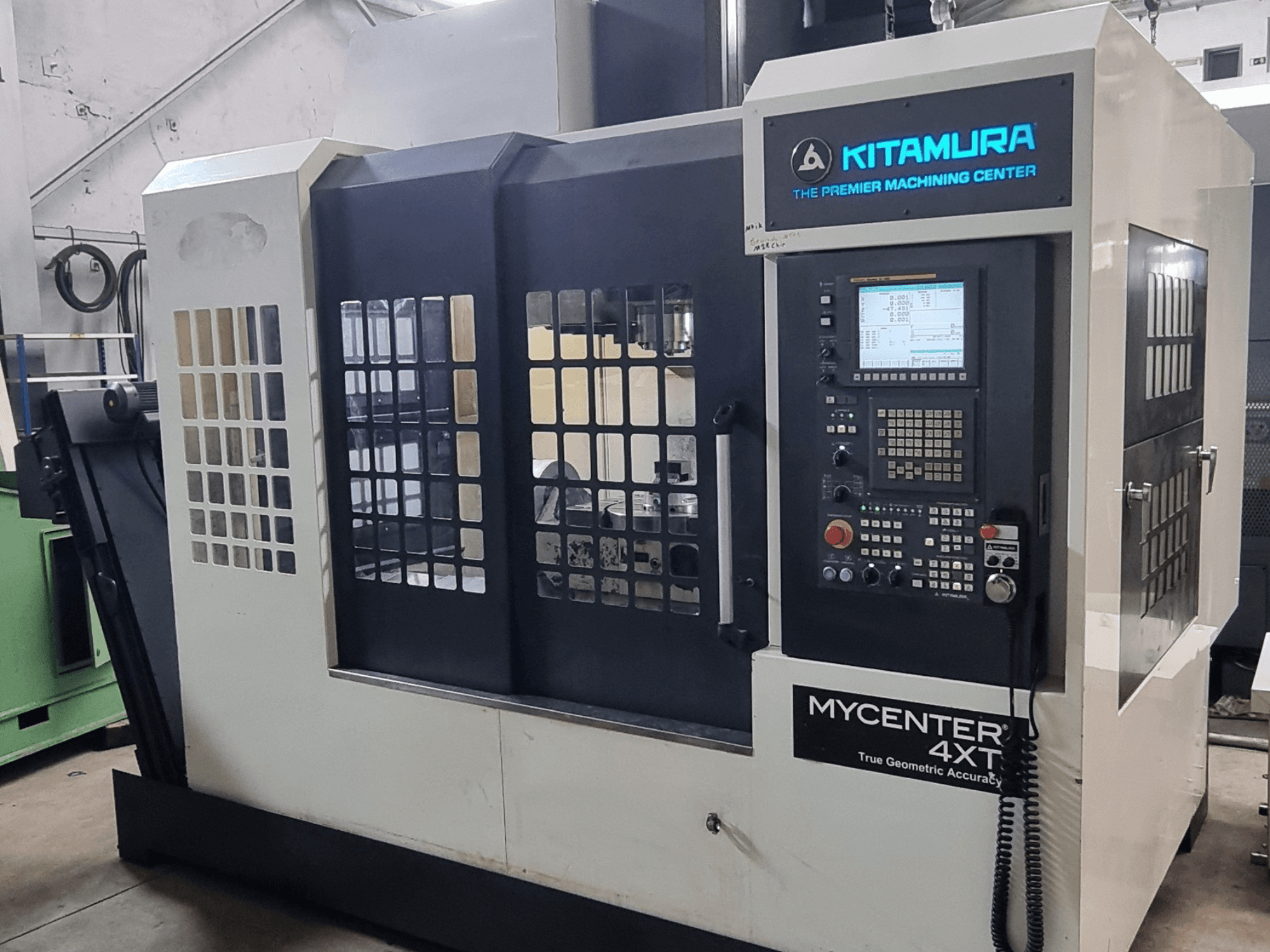 Texte alternatif : Centre d'usinage vertical Kitamura MYCENTER 4XT, vue de face, mettant en avant le panneau de commande et les détails de la machine dans un atelier.