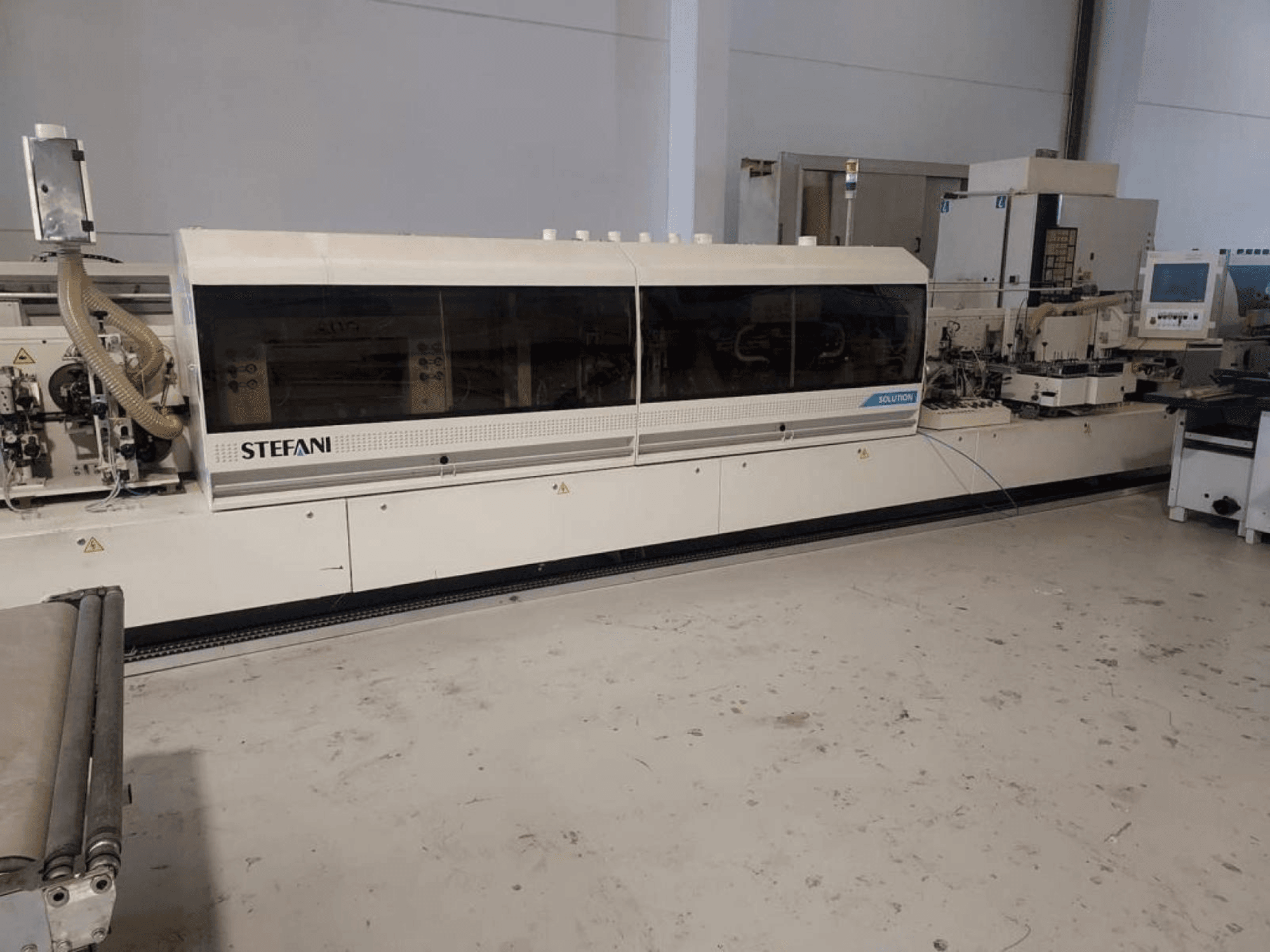 Plaqueuse de chants Stefani Solutions, vue de face, avec système d'aspiration des poussières et panneau de commande visible, dans un atelier.