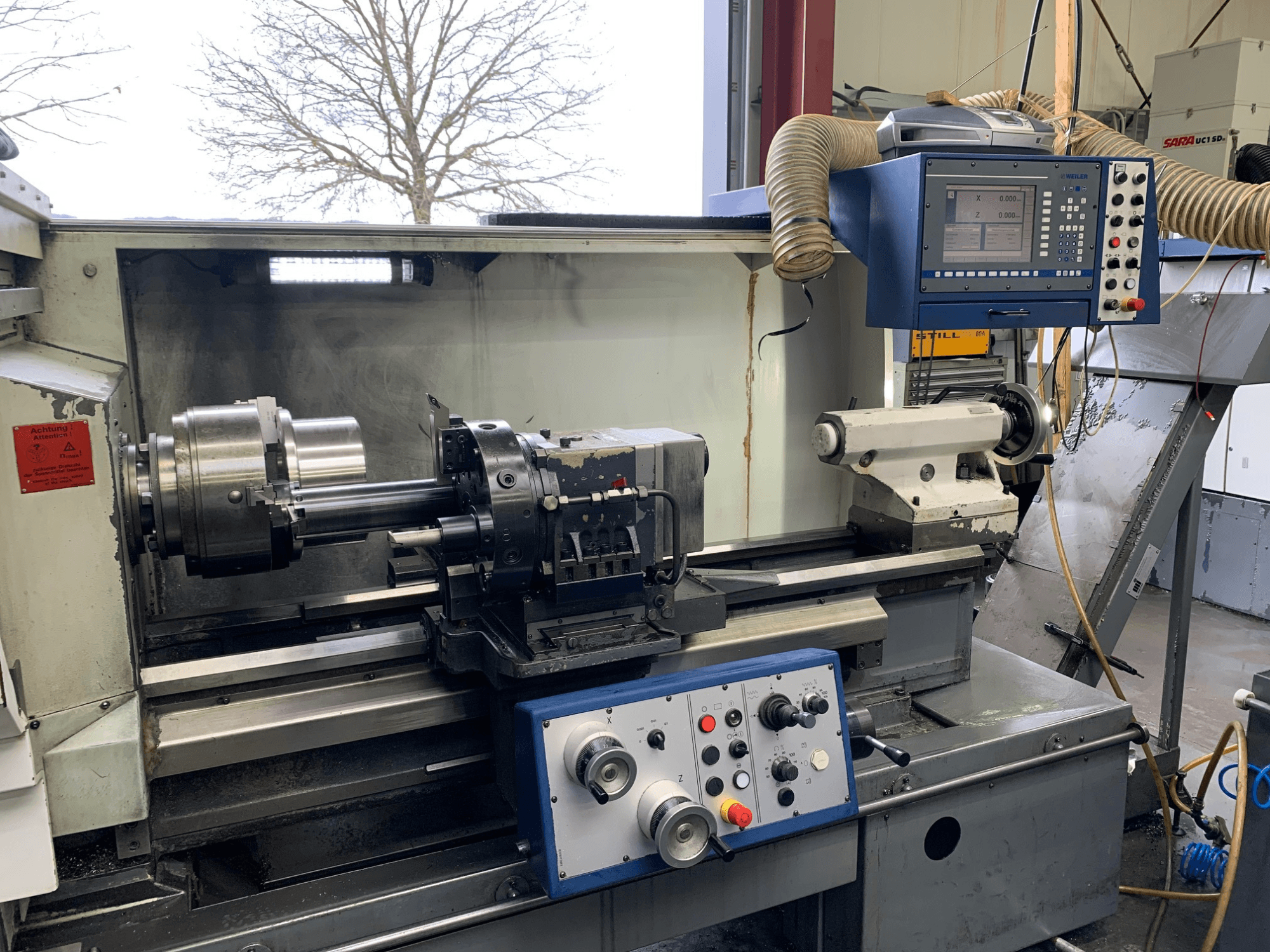 Tour horizontal Weiler E55X1000 dans un atelier, montrant le panneau de commande, le tour et le porte-outil. Vue de face.