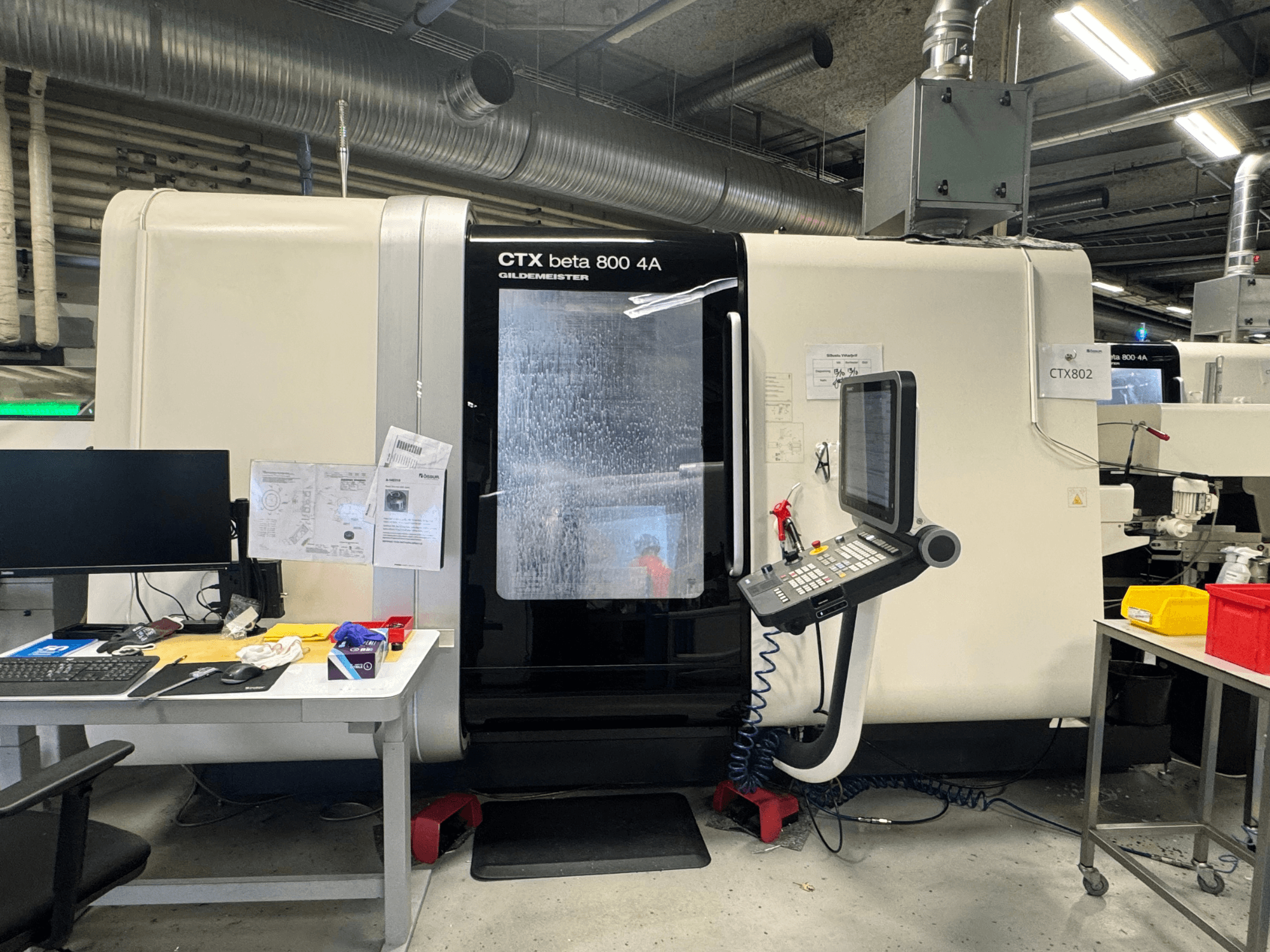 Machine CNC CTX beta 800 4A dans un atelier, vue latérale montrant le panneau de commande et l'espace de travail encombré d'outils et de documents.