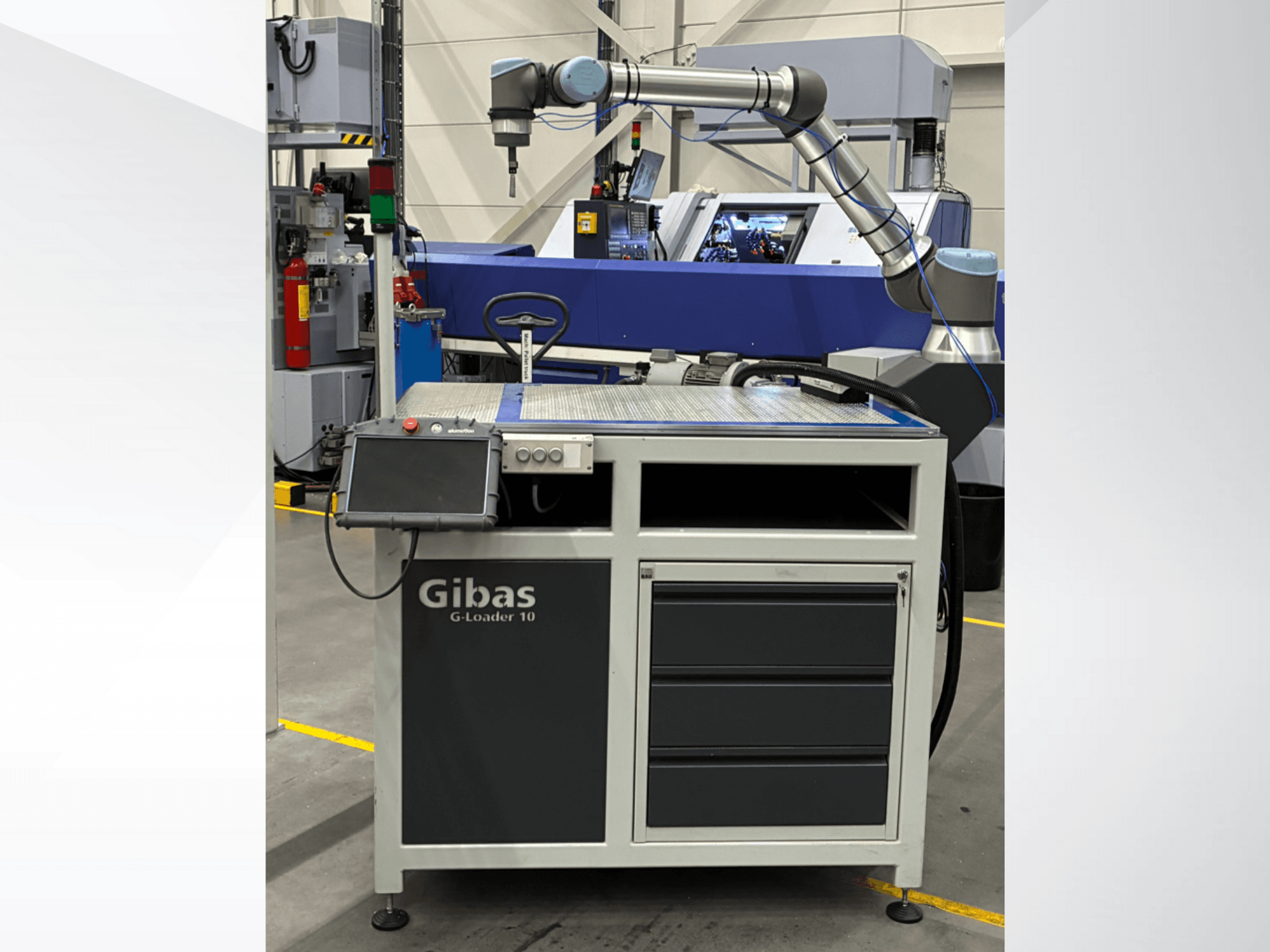 Gibas G-Loader 10 avec bras robotisé, vue de face ; commande par écran tactile et tiroir de rangement dans un environnement industriel.