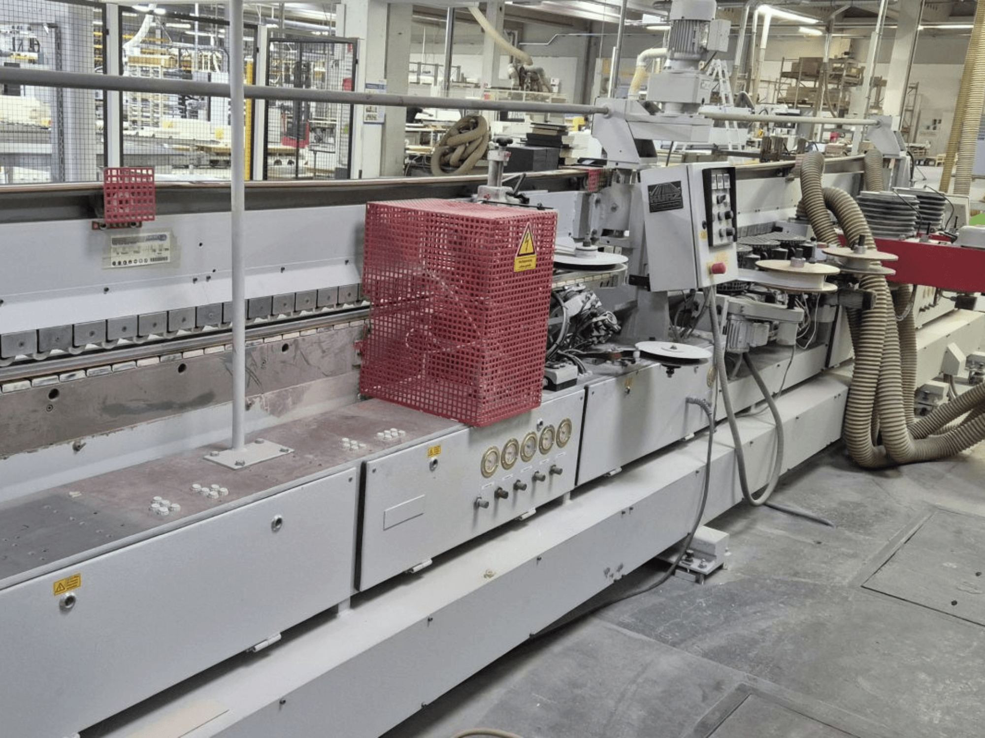 Plaqueuse de chants avec panneau de commande, tuyaux d'aspiration et couvercle de sécurité rouge, vue de côté.