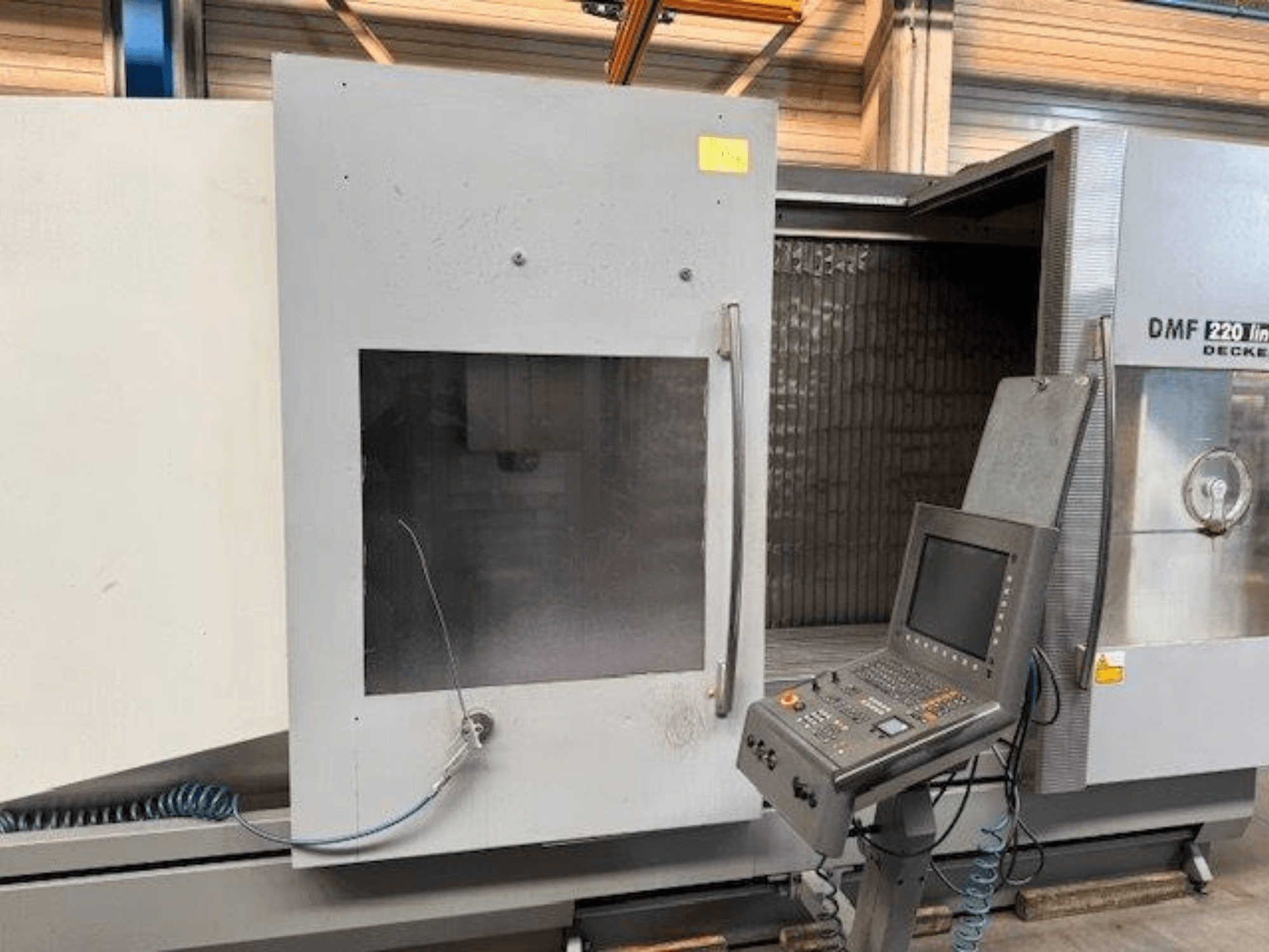 Vue avant du centre d'usinage vertical DECKEL MAHO DMF 220 Linear, montrant le panneau de commande et la porte ouverte de la machine.