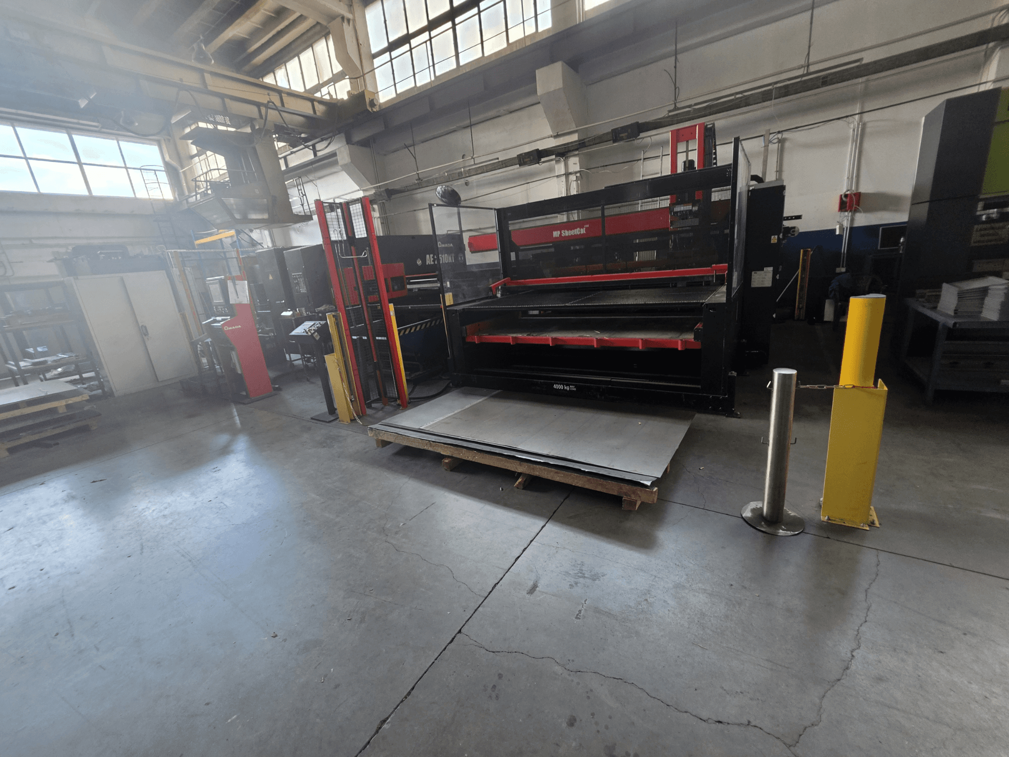 Poinçonneuse CNC AMADA AE-2510NT dans l'entrepôt, vue de profil, montrant la configuration de la machine et les tôles.