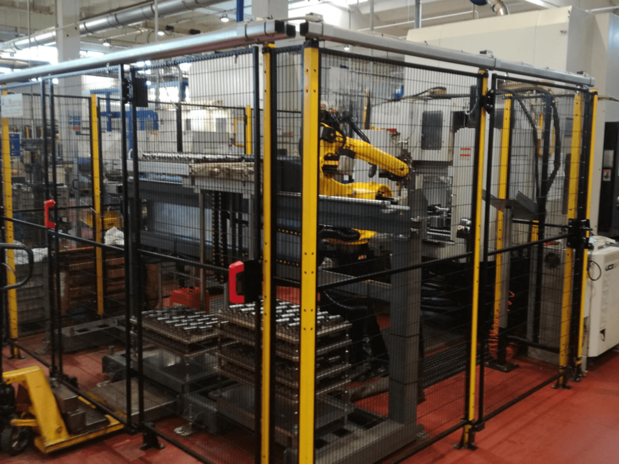 Centre d'usinage vertical Enshu EV450 dans un espace de travail clôturé, avec des bras robotisés et plusieurs pièces empilées. Vue de face.