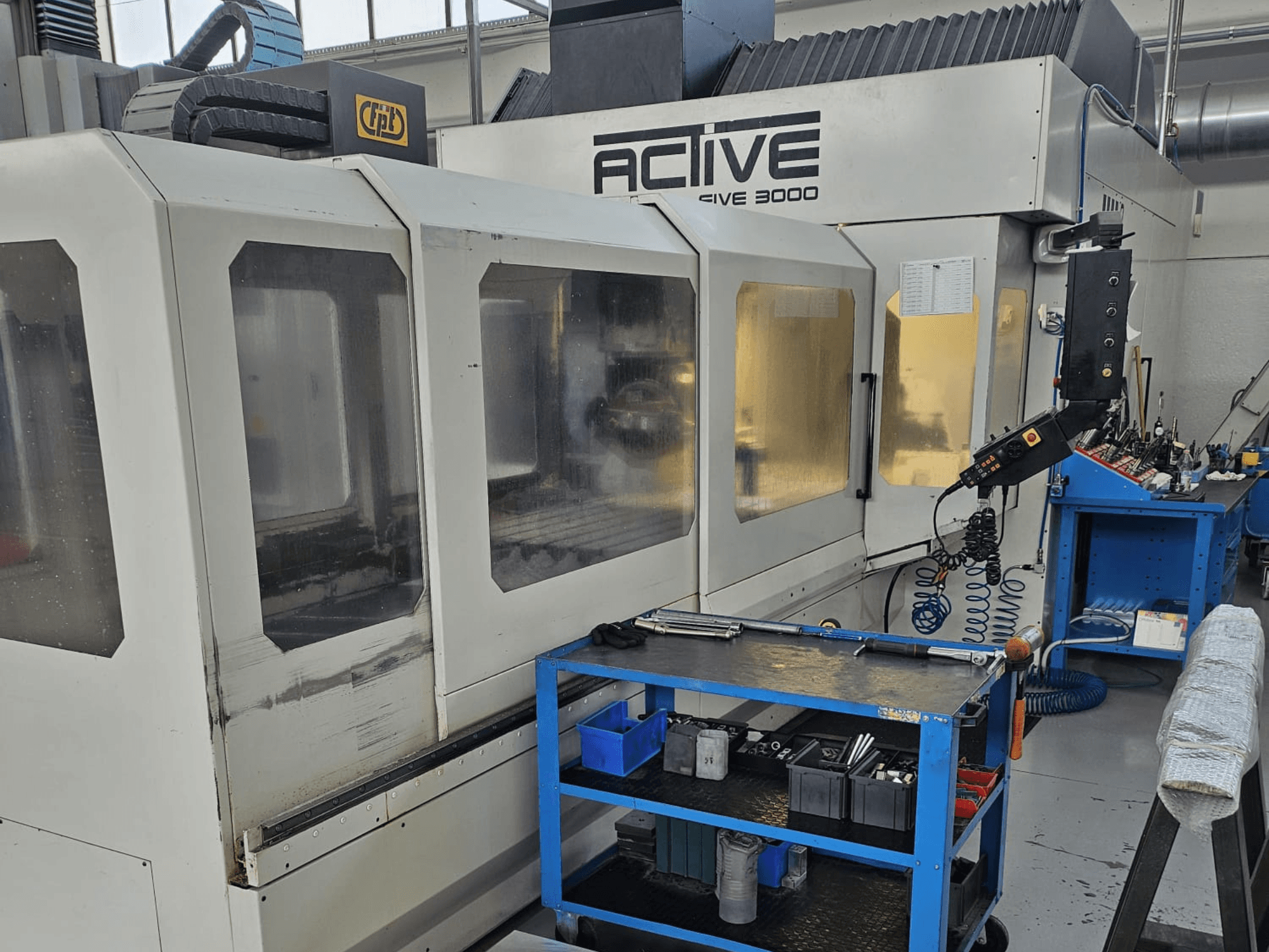 Machine CNC 3000 active dans un atelier, vue de face avec des outils sur un chariot bleu, commandes visibles et zone de travail à l'intérieur.