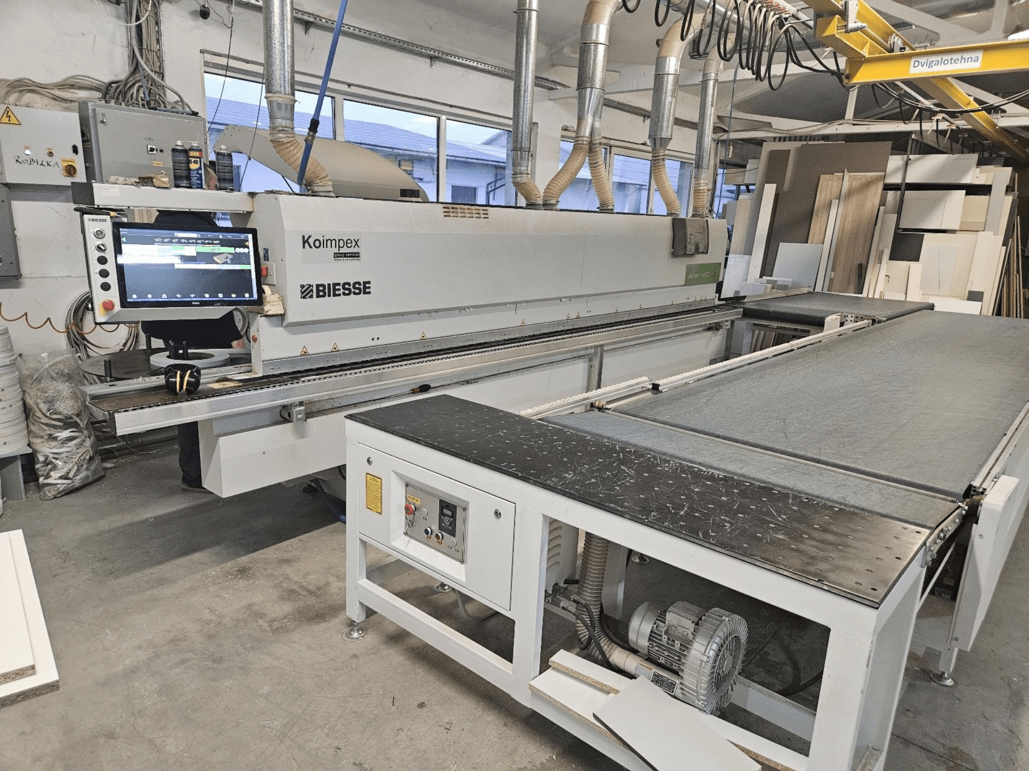 BIESSE Akron 1440 Une plaqueuse de chants dans un atelier, vue latérale montrant le panneau de commande et la bande transporteuse.