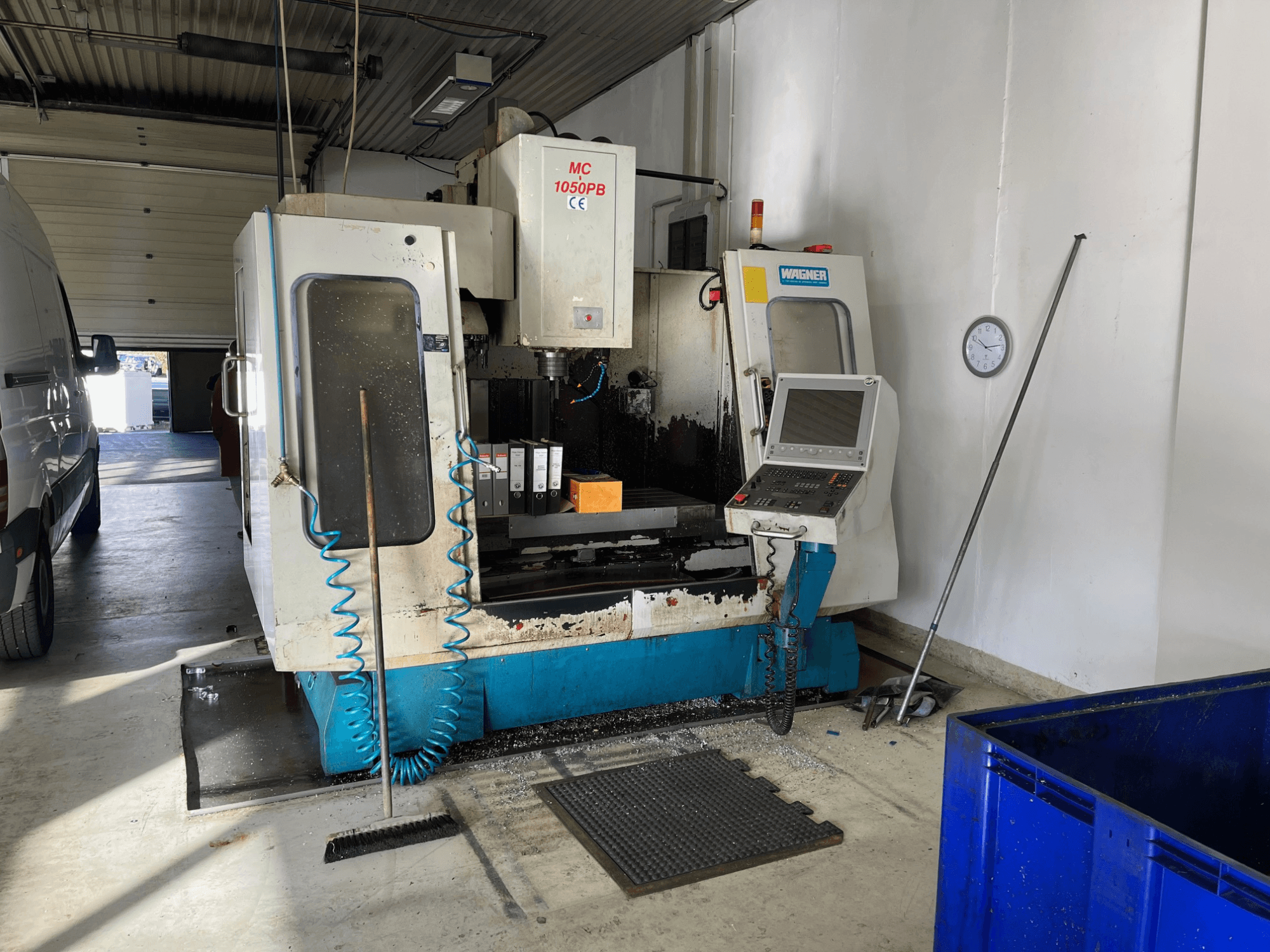Machine CNC WAGNER MC 1050PB dans l'atelier, vue de face, avec le panneau de commande et la zone de travail ; le tuyau d'air bleu et les outils de nettoyage sont visibles.