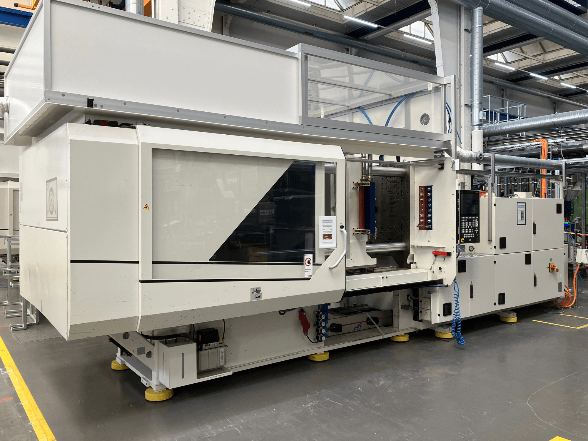 Vue latérale d'une machine de moulage par injection, modèle AET, dotée d'un panneau de commande et de couvercles transparents, dans un environnement industriel.