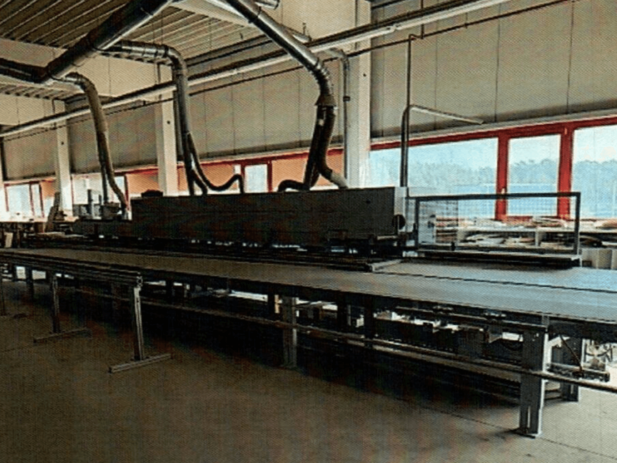 Plaqueuse de chants HOMAG KAL 370 dans un atelier, vue de côté, montrant la longue table de travail plate avec les conduits de ventilation au-dessus.