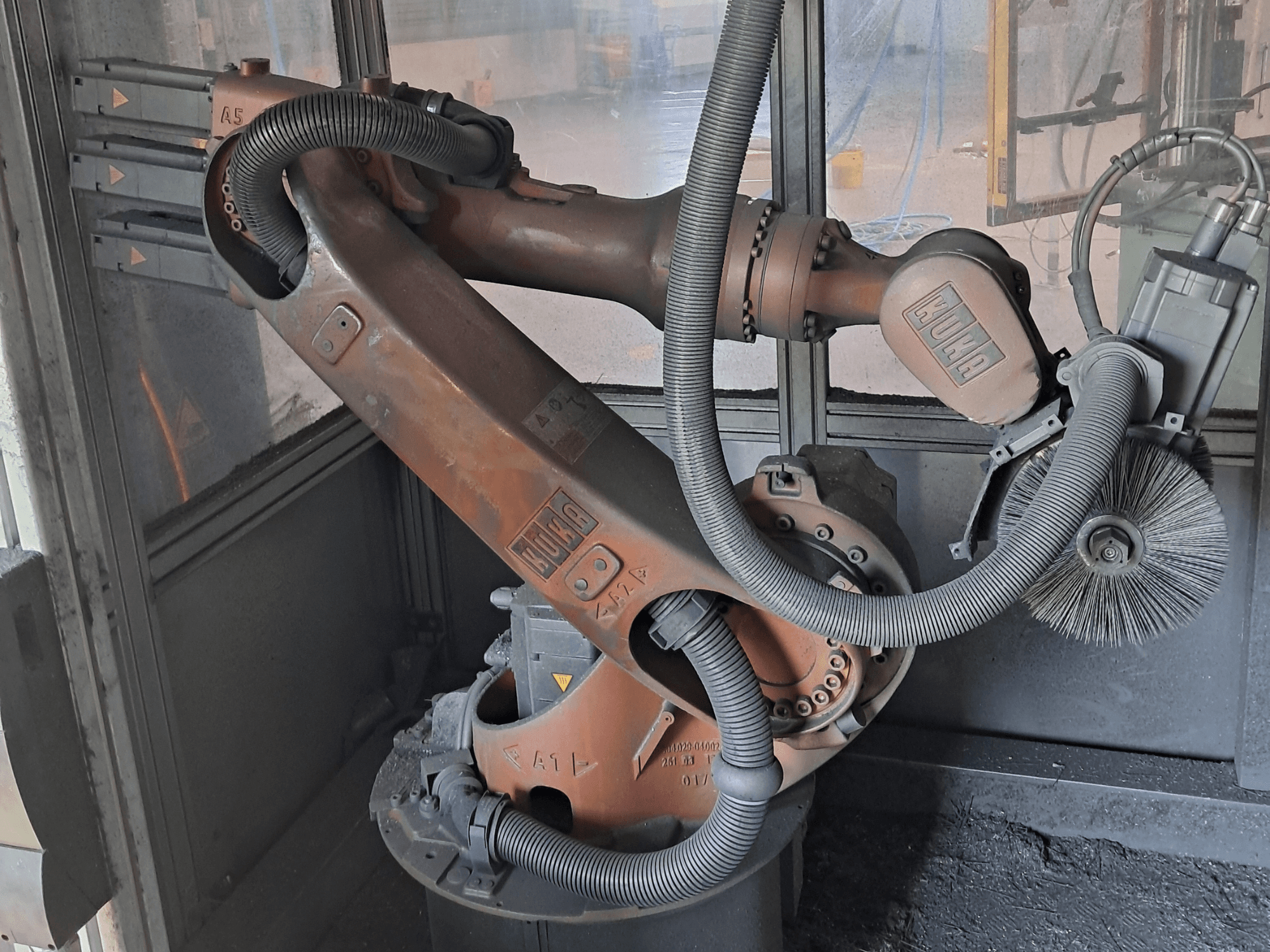 Vue de profil du bras robotisé KUKA KR 16-2, mettant en évidence les câbles, les balais et les articulations mécaniques, dans un environnement de travail.