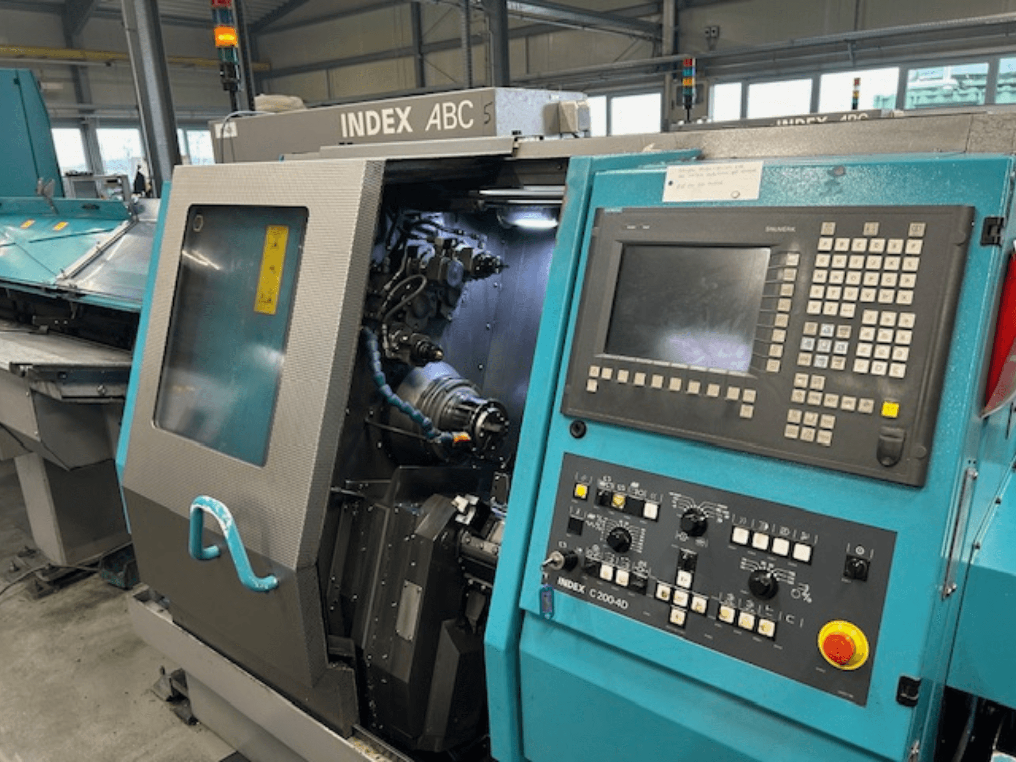 Vue avant d'un tour CNC INDEX C200-AD avec panneau de commande, composants internes visibles et dispositifs de sécurité.