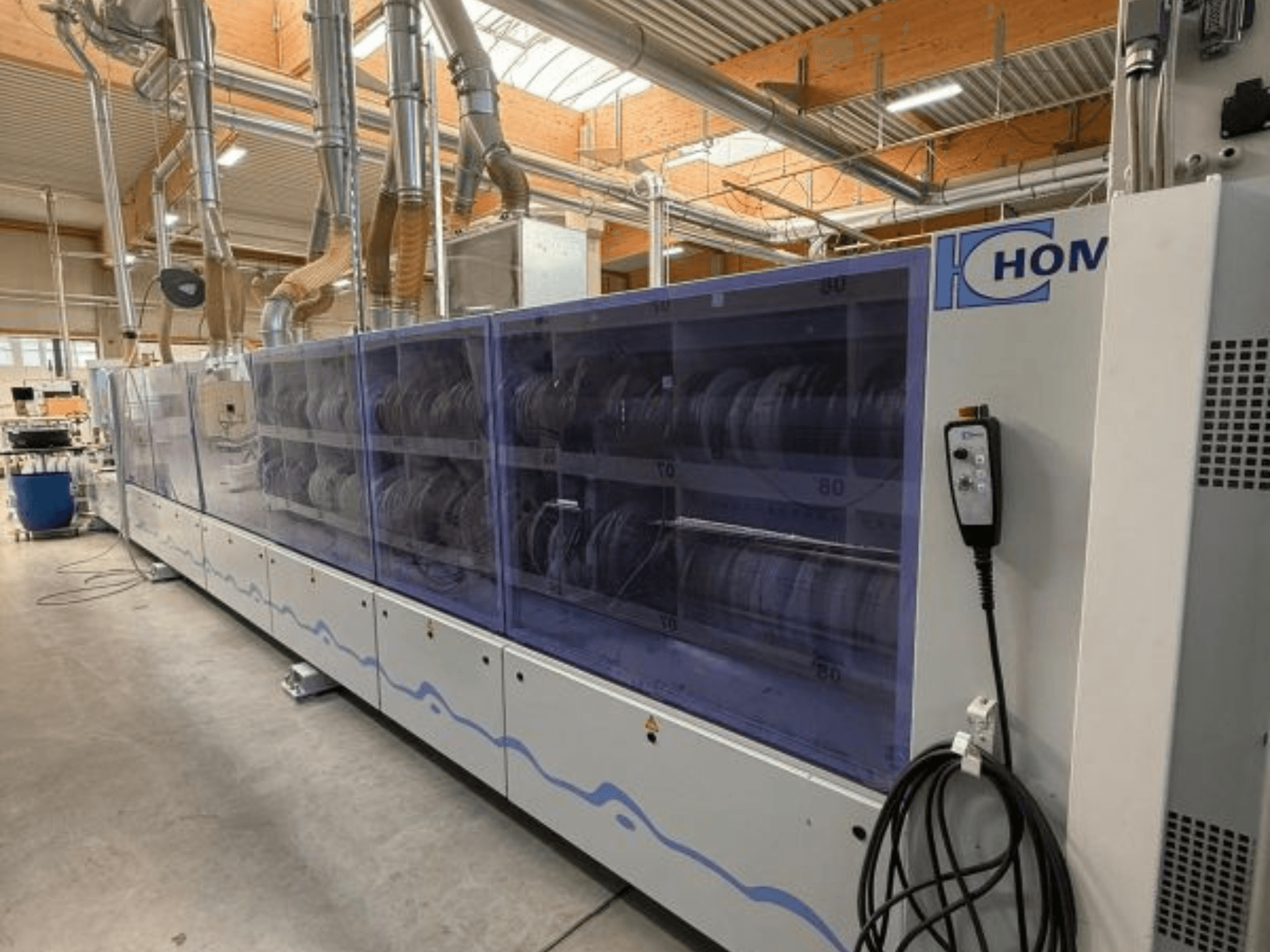 Machine à laver industrielle HOM, vue de face, avec panneau transparent présentant la vaisselle ; panneau de commande avec boutons sur le côté.