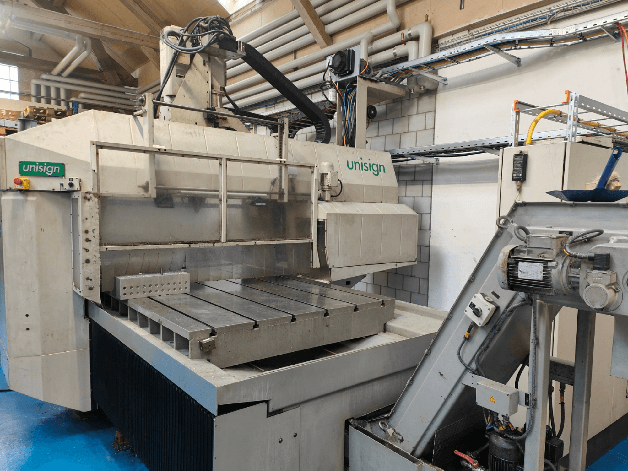 Machine CNC Unisign dans un atelier, vue de face, avec une grande table, un panneau de commande et des éléments de design industriel.