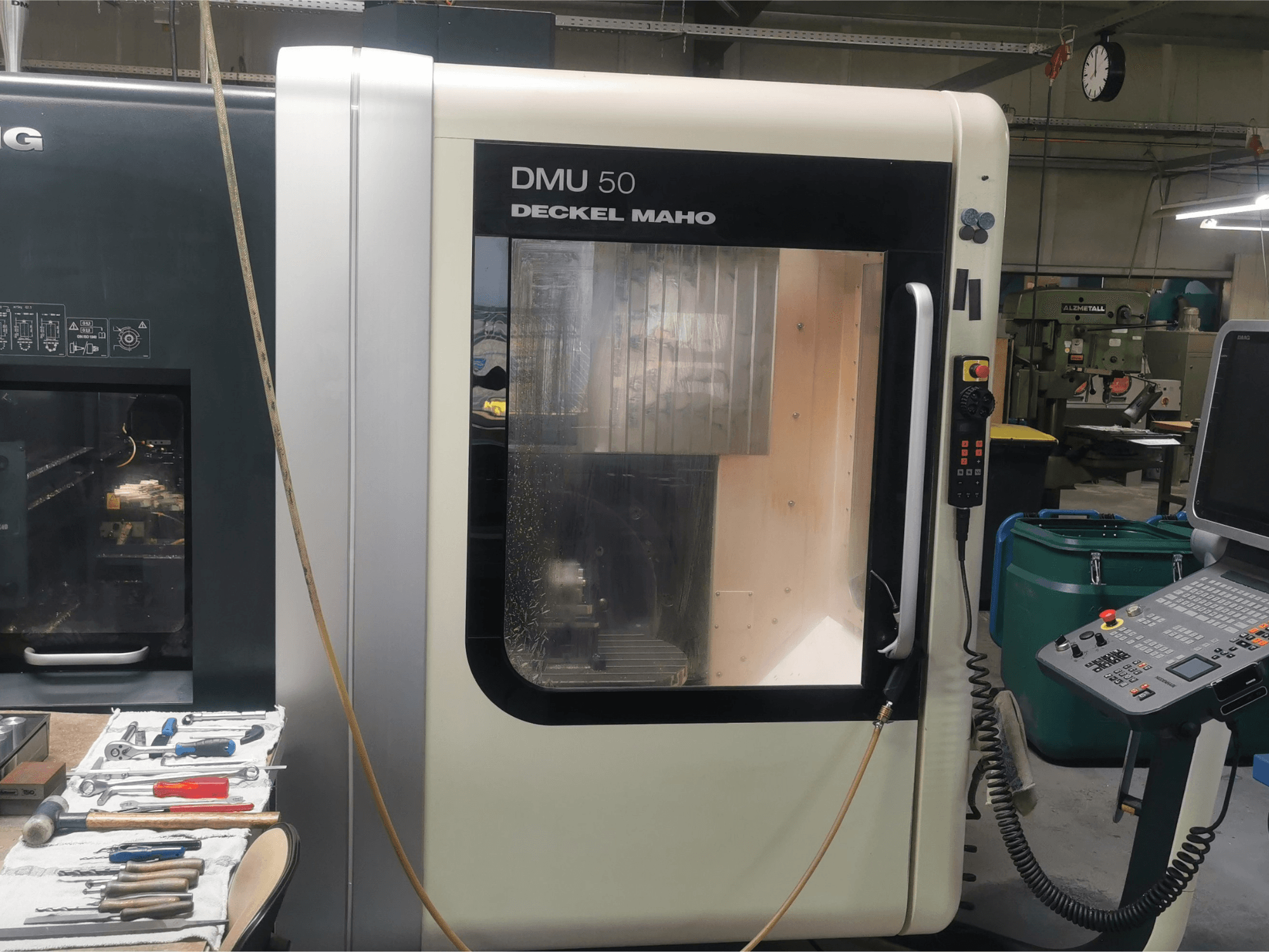 Machine CNC DMU 50 deckel maho vue de face, avec son panneau de commande et sa porte transparente. Les outils sont à proximité.