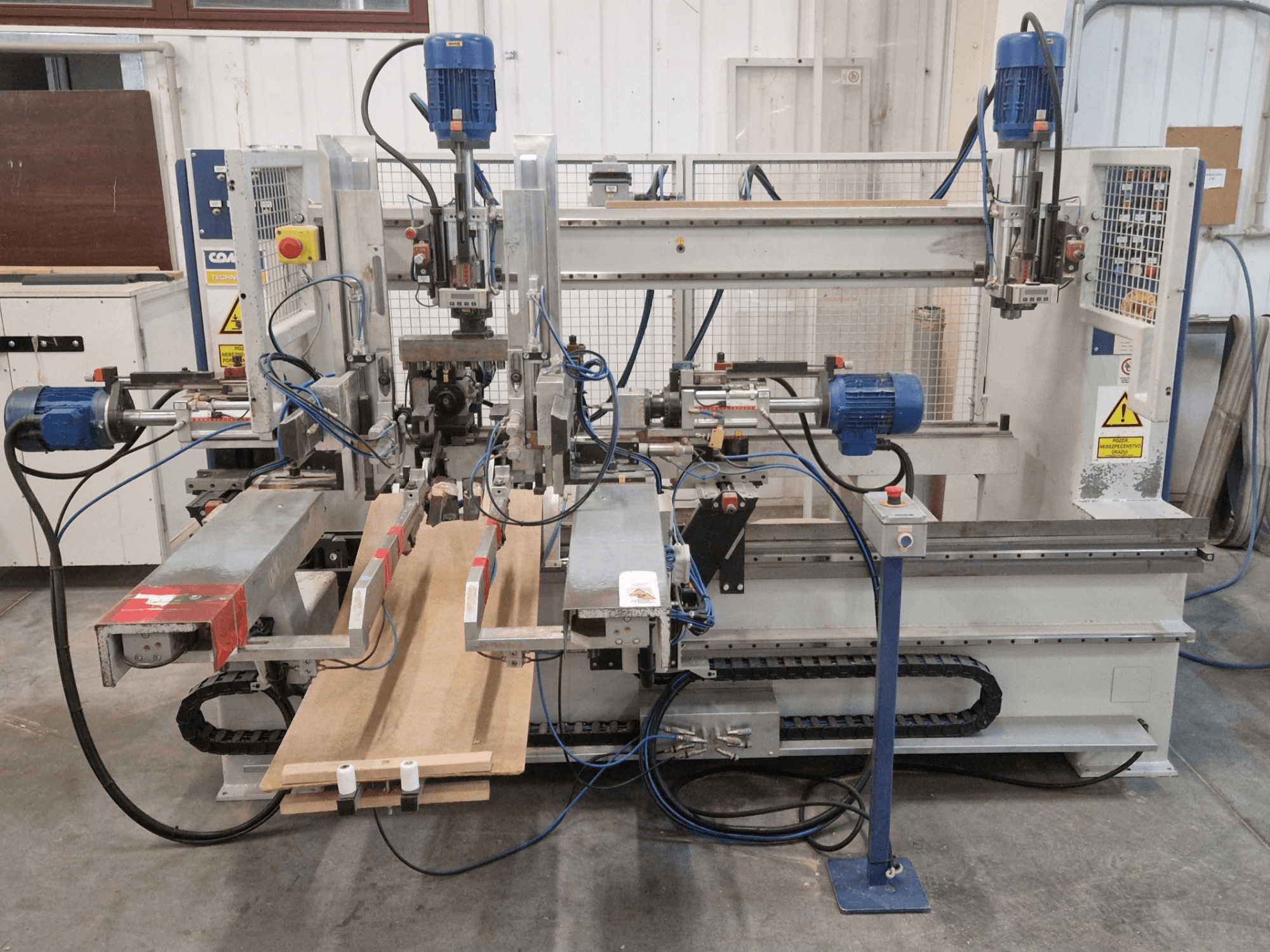 Vue de face de la perceuse multibroche COMEC FMOV 1500, montrant les deux broches, le panneau de commande et la pièce de bois en fonctionnement.