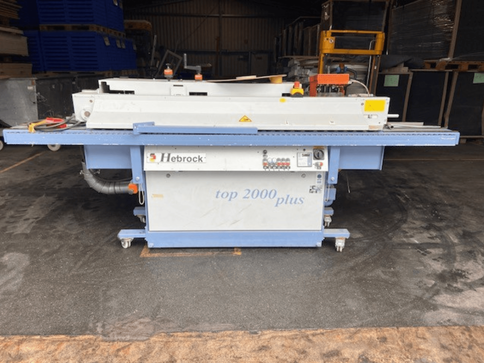Hebrock Top 2000 Plus, vue de face ; machine industrielle électrique avec panneau de commande, roues pour la mobilité et étiquettes de sécurité visibles.