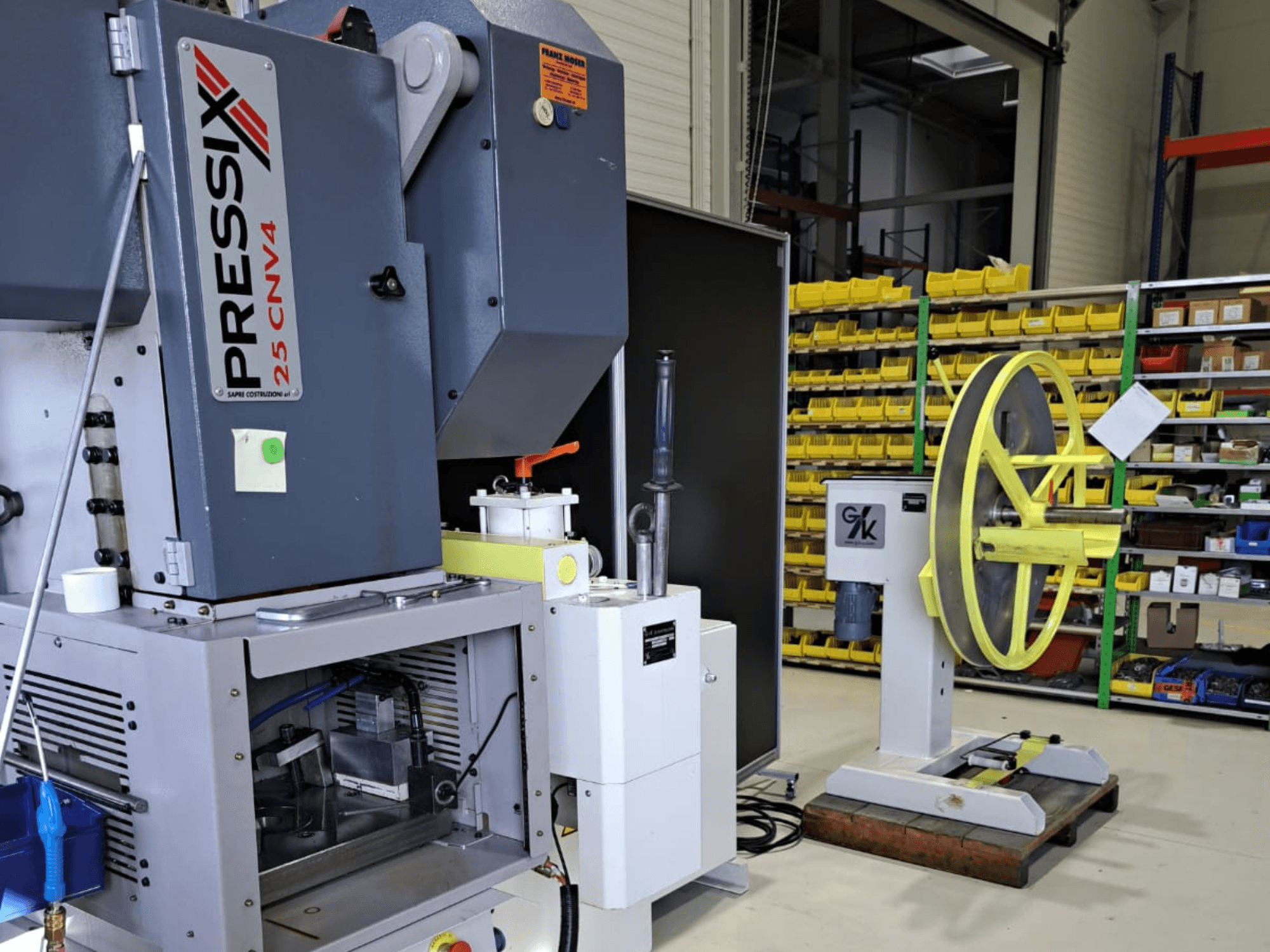 Installation d'une machine industrielle comprenant PRESSIX 25 CNV4 à gauche et une roue jaune montée sur une base grise à droite, vue de face.