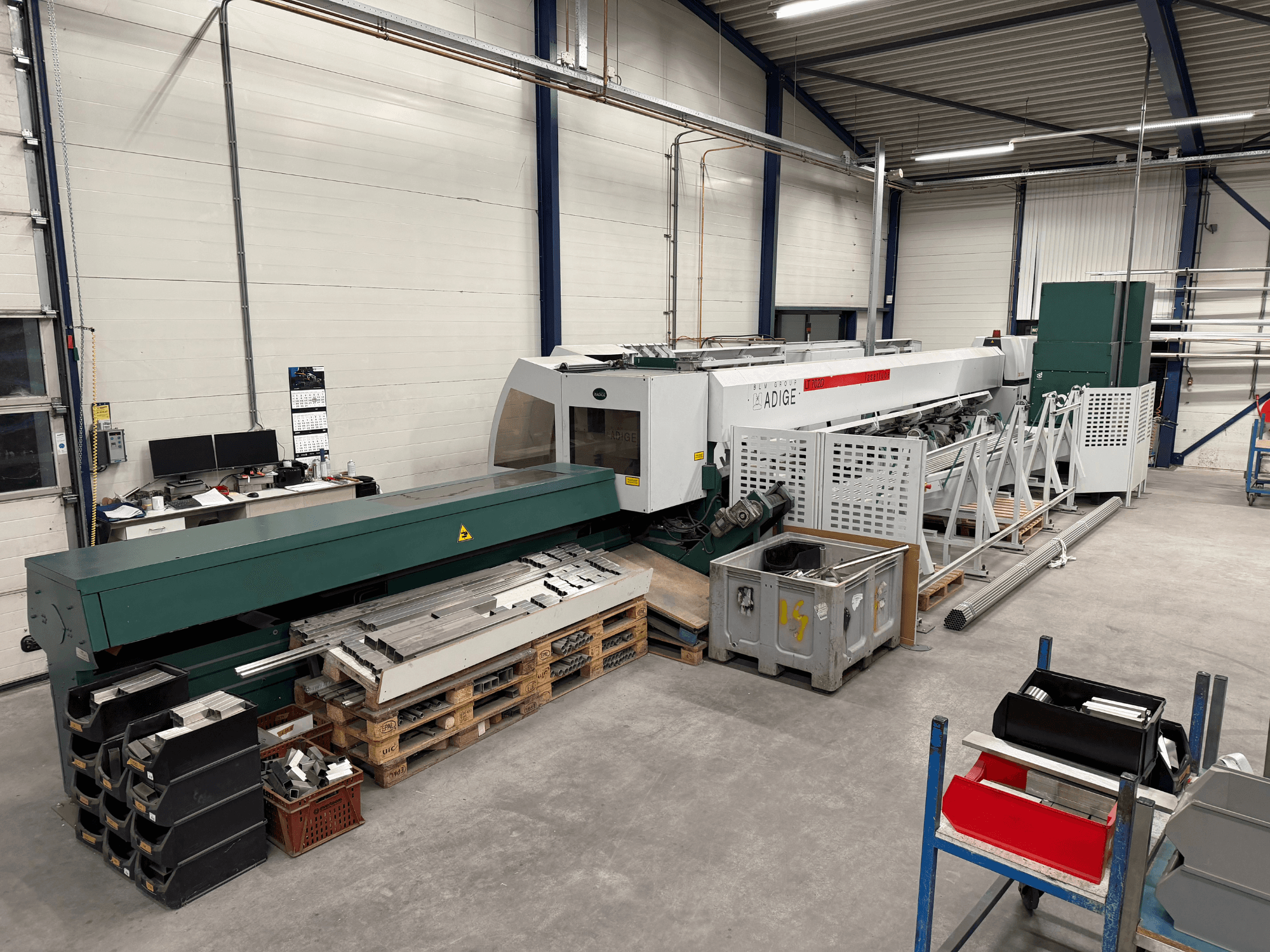 Machine de découpe laser CO₂ BLM Adige LT702 dans un atelier, vue de profil montrant les composants métalliques et l'encombrement de l'espace de travail.