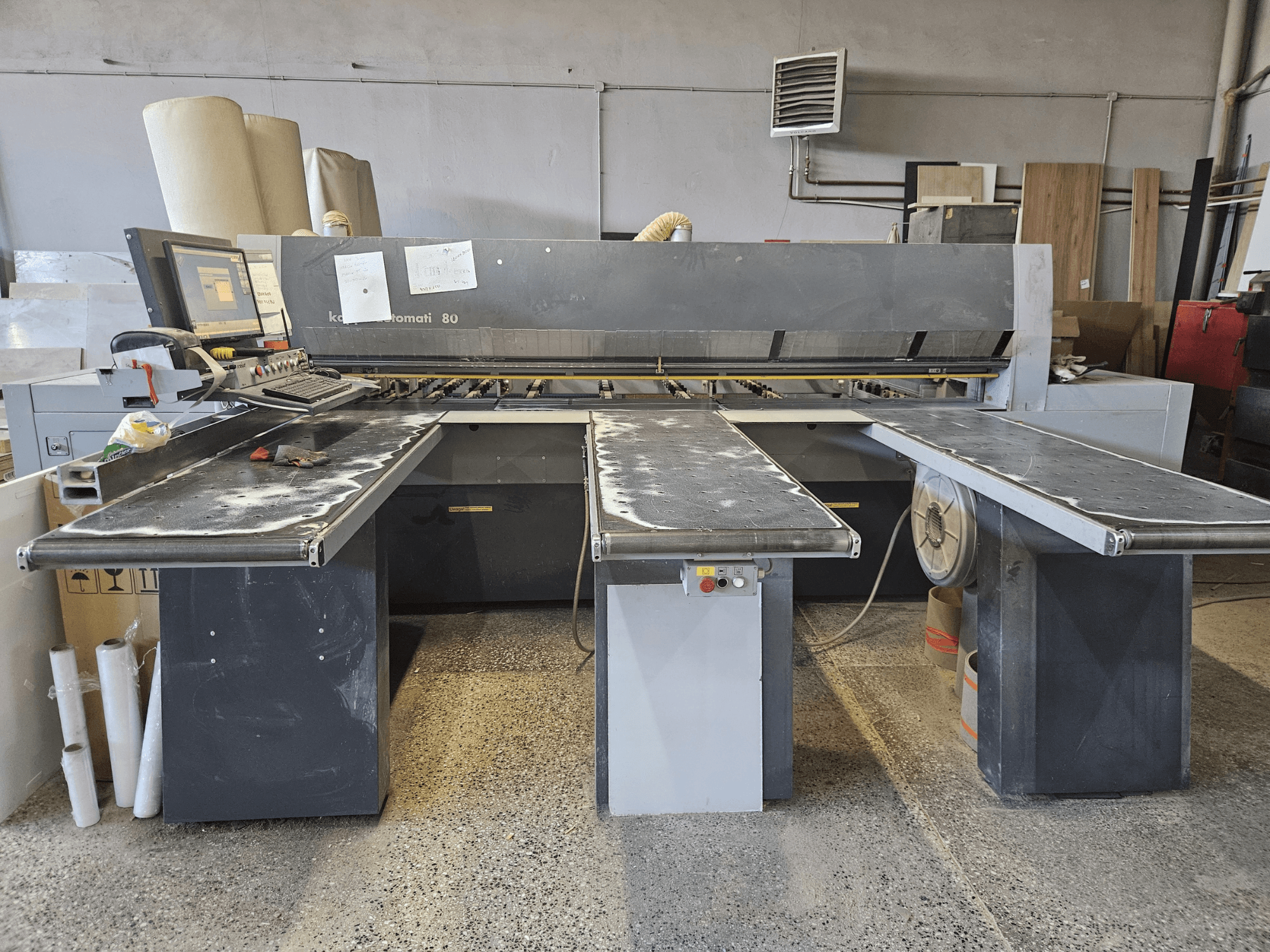 Machine KAPPA Automati 80, vue de face, avec trois tables plates, un panneau de commande et de la sciure éparpillée sur les surfaces.